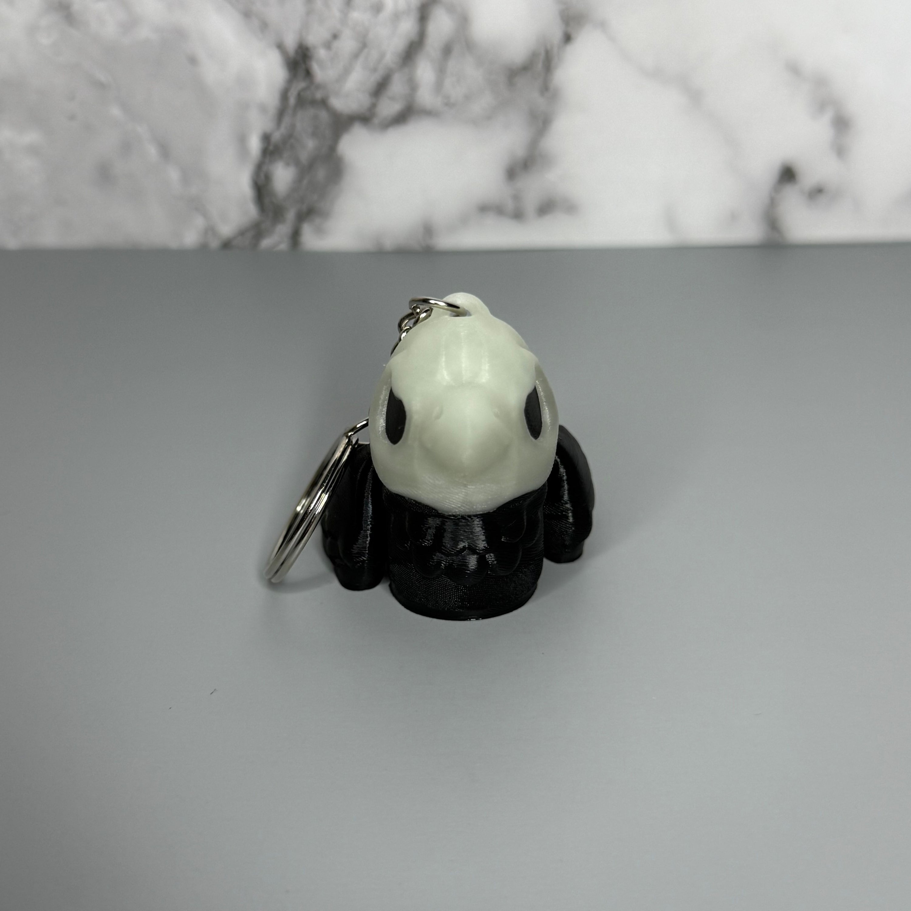Black and white crow-shaped keychain with crow-shaped skull head on light gray background