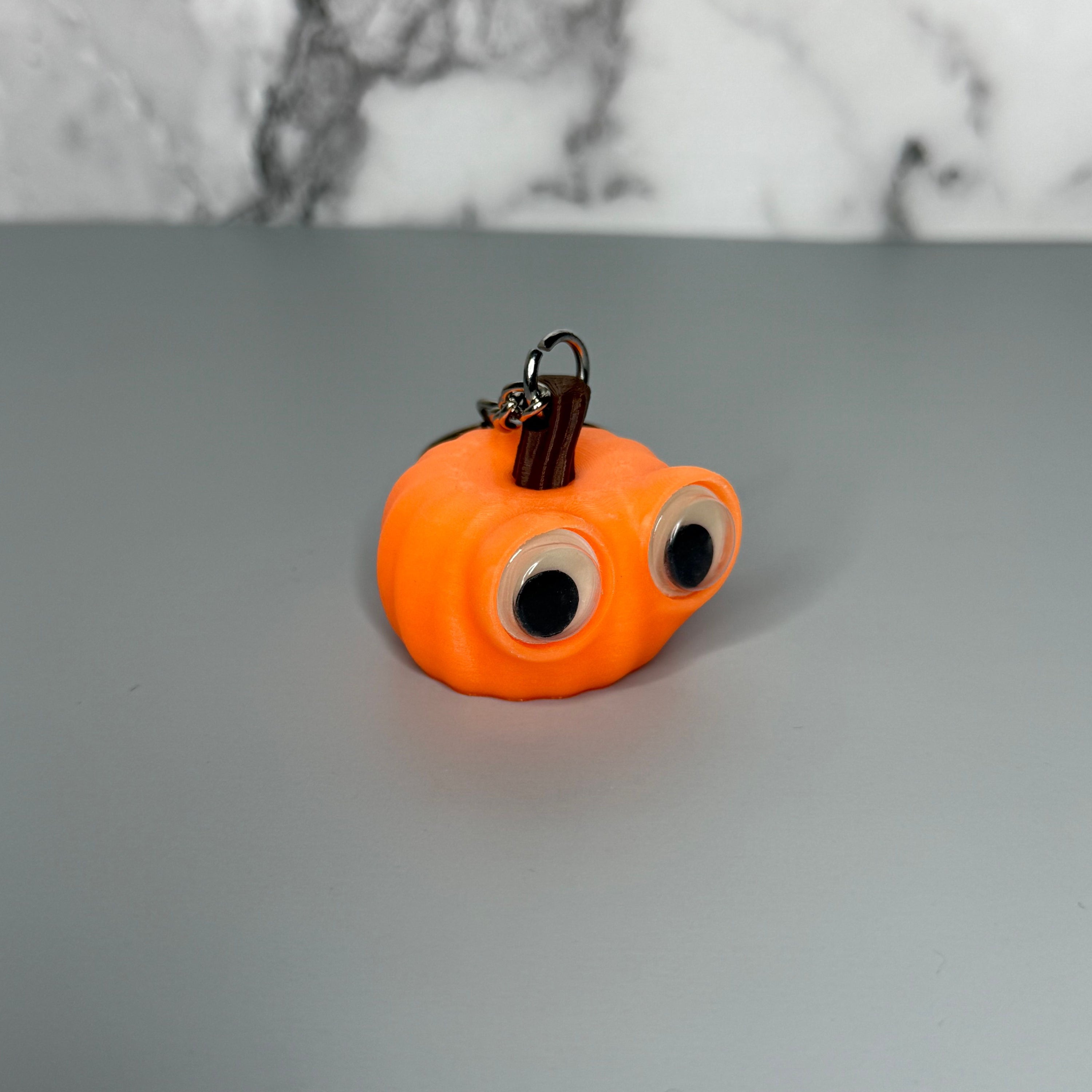 Orange pumpkin-shaped keychain with googly eyes on a gray background