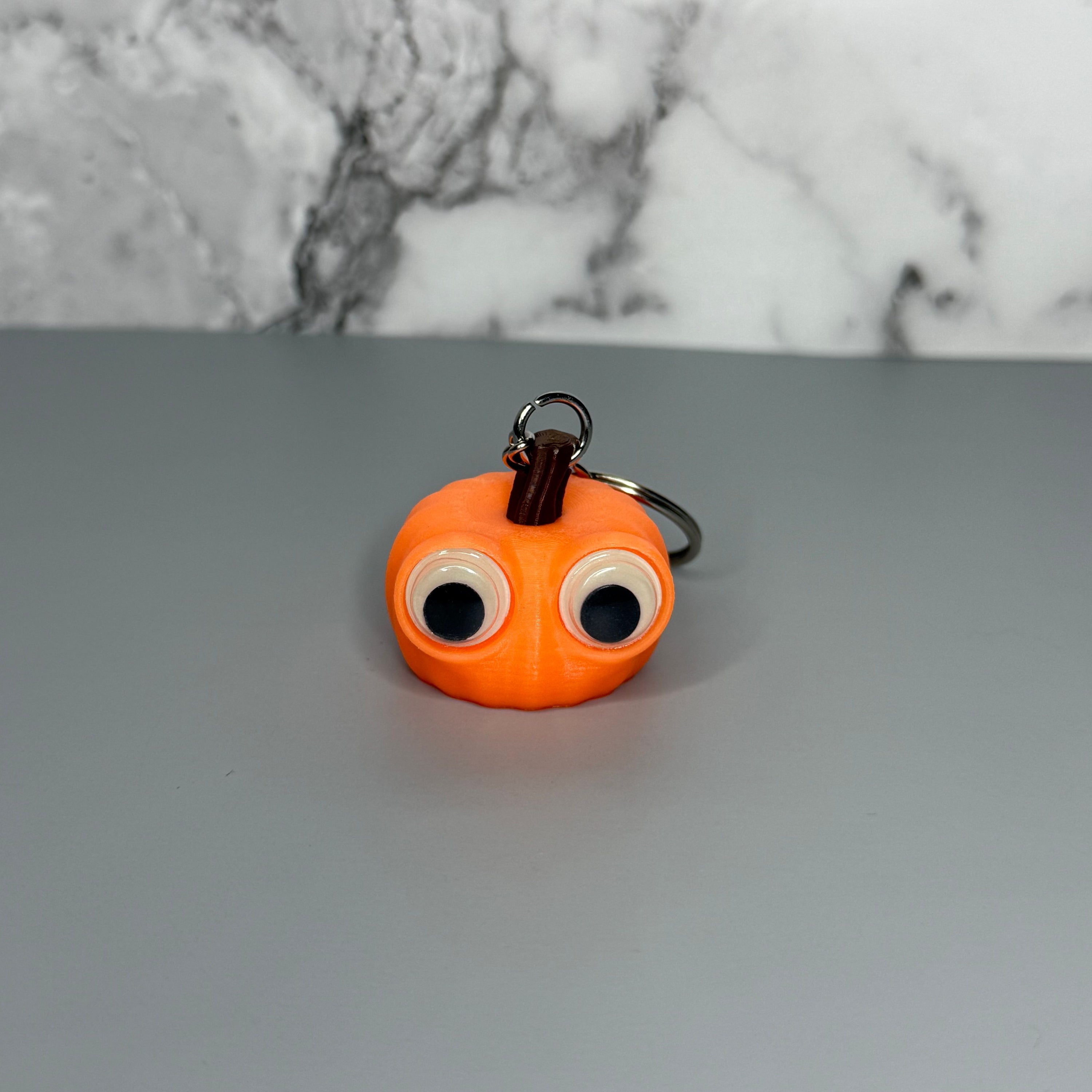Orange pumpkin-shaped keychain with googly eyes on a gray background