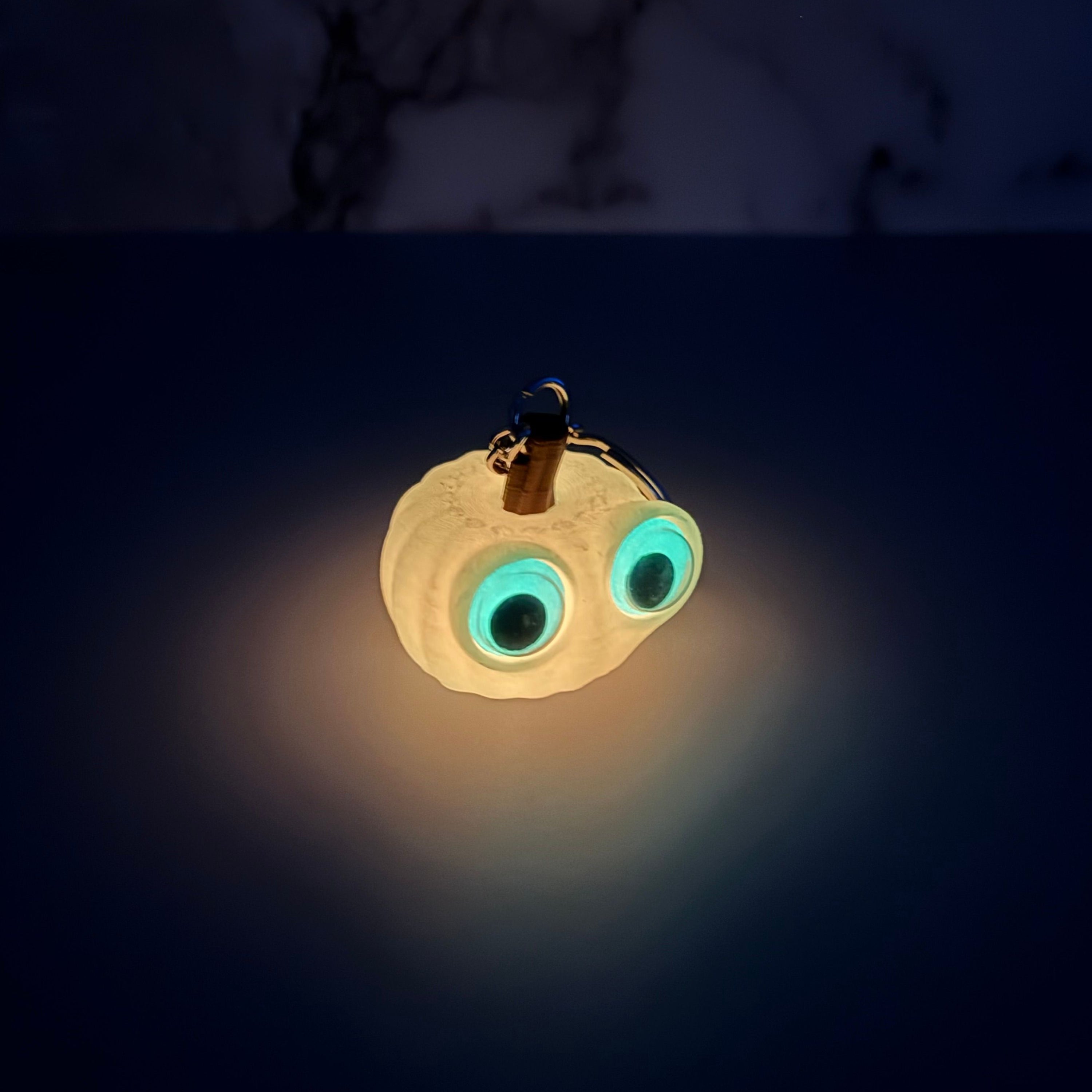 Glowing orange pumpkin-shaped keychain with googly eyes on a gray background