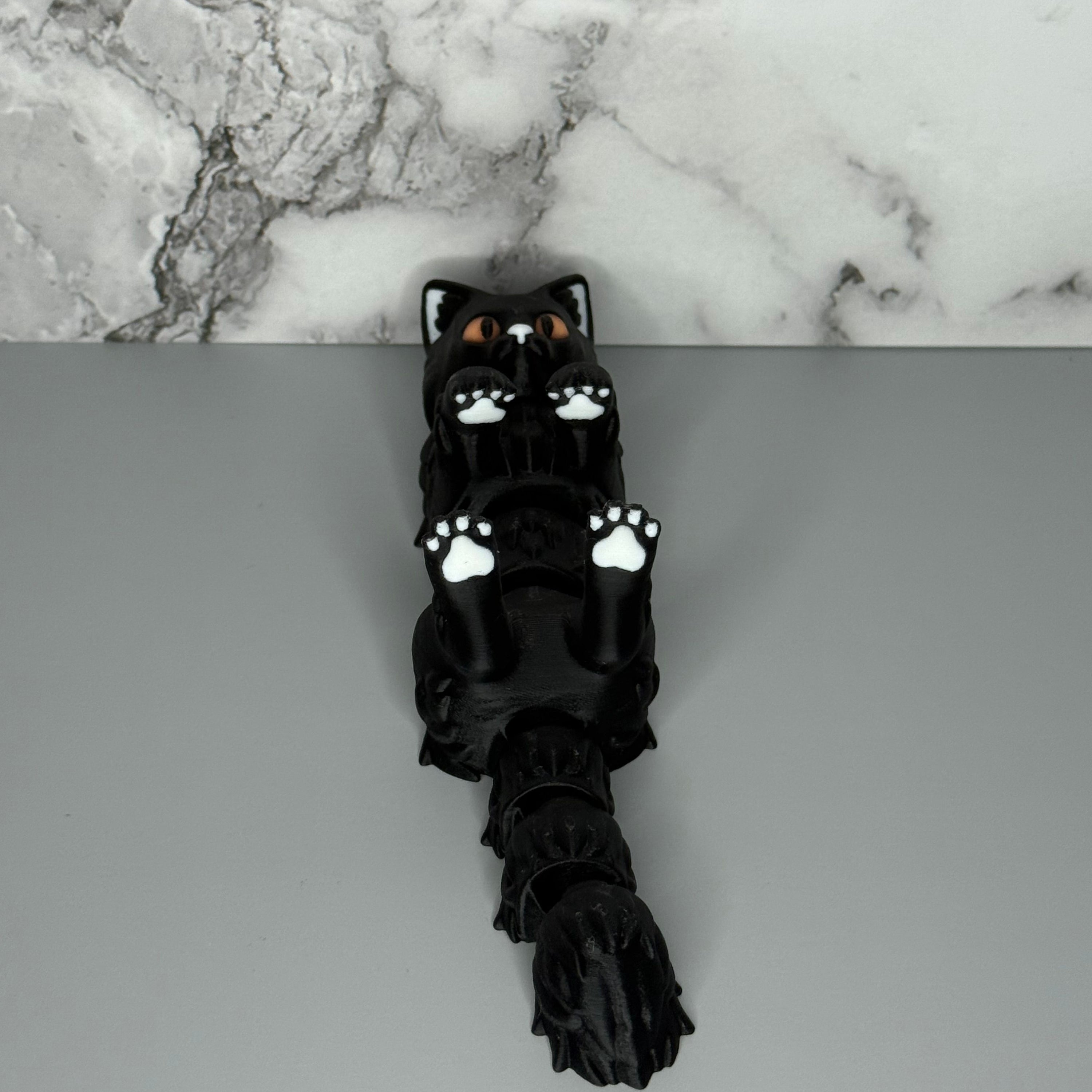 Black cat-shaped figure with white paws on a gray and marble surface