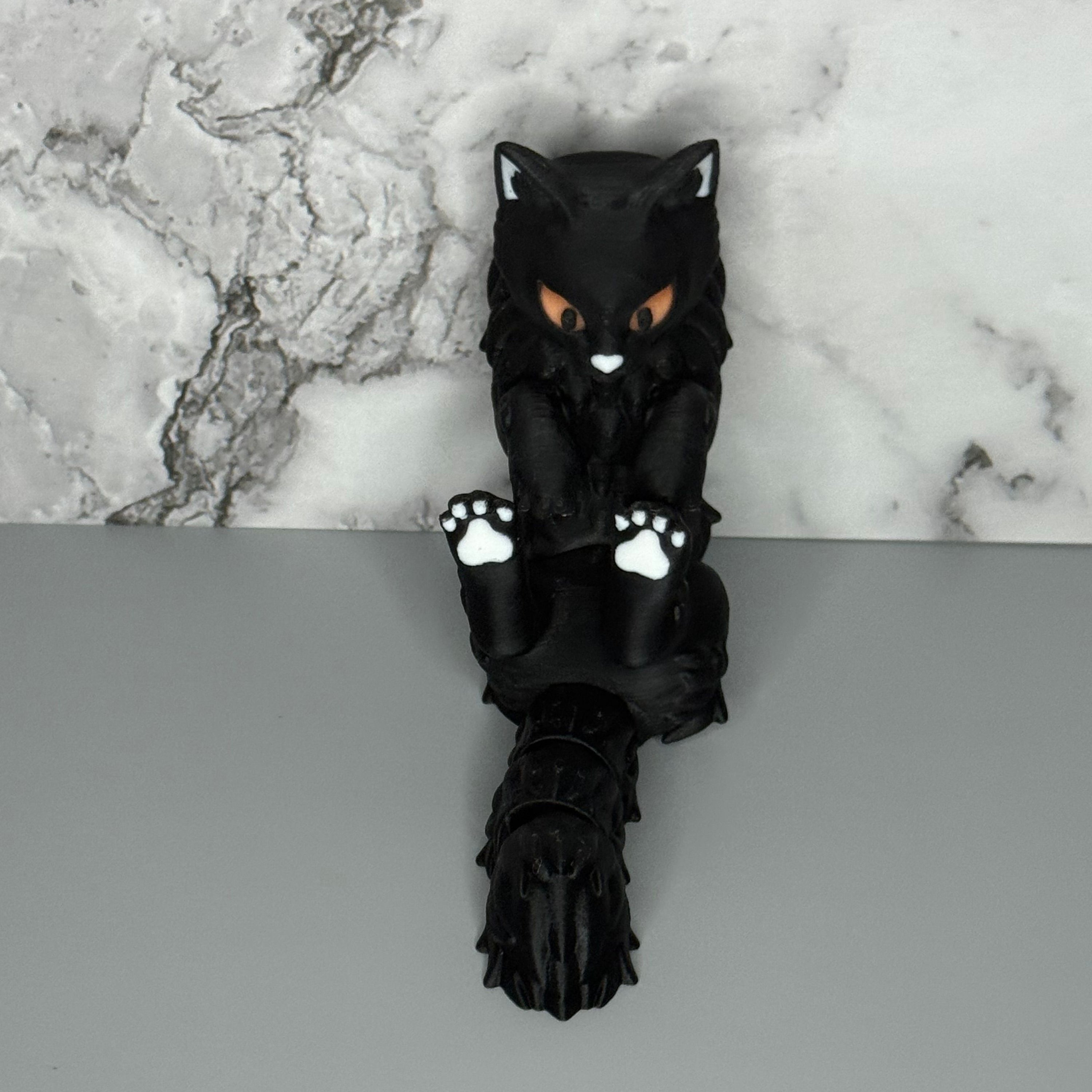 Black cat-shaped figure with white paws on a gray and marble surface