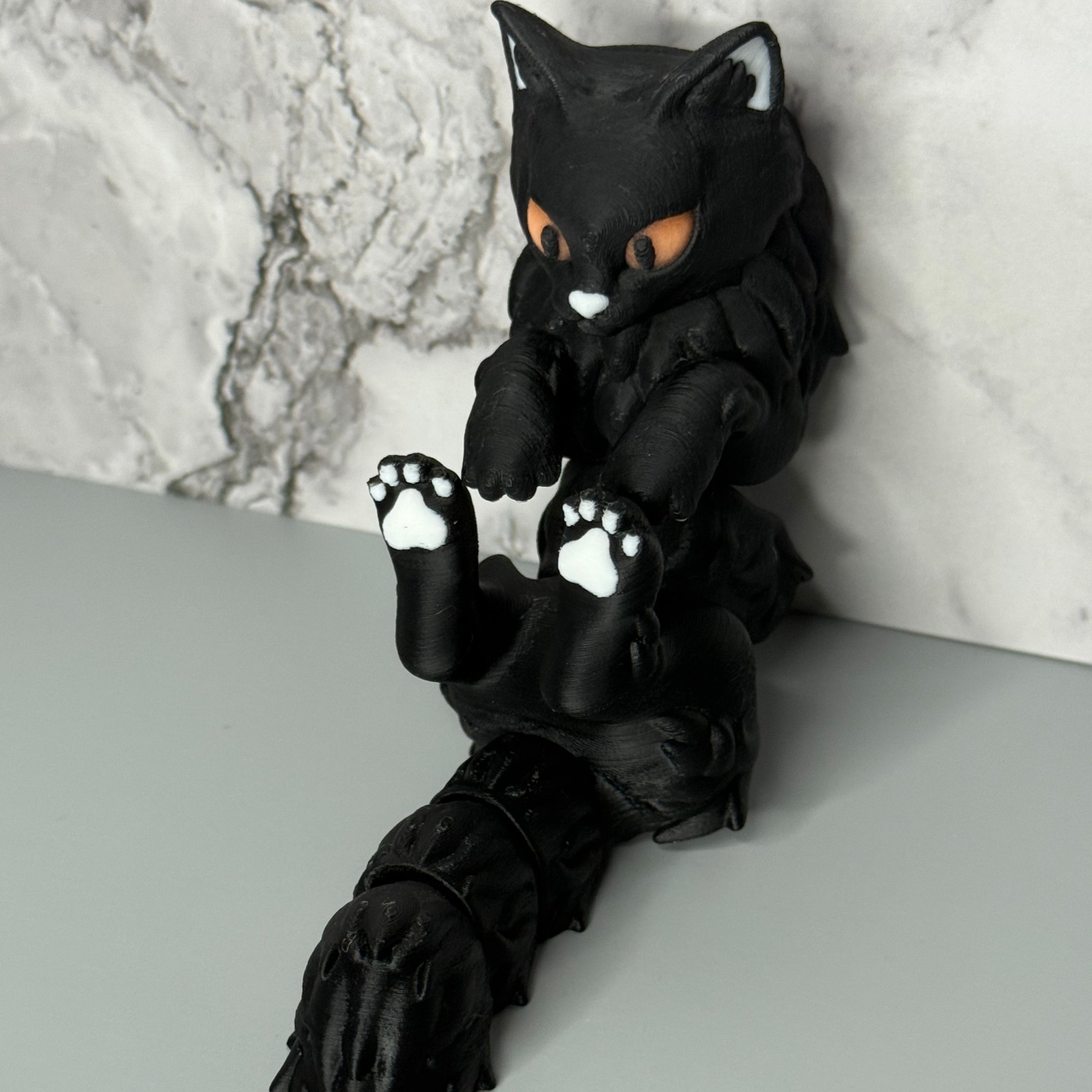 Black cat-shaped figure with orange eyes and white paws on a gray and marble surface