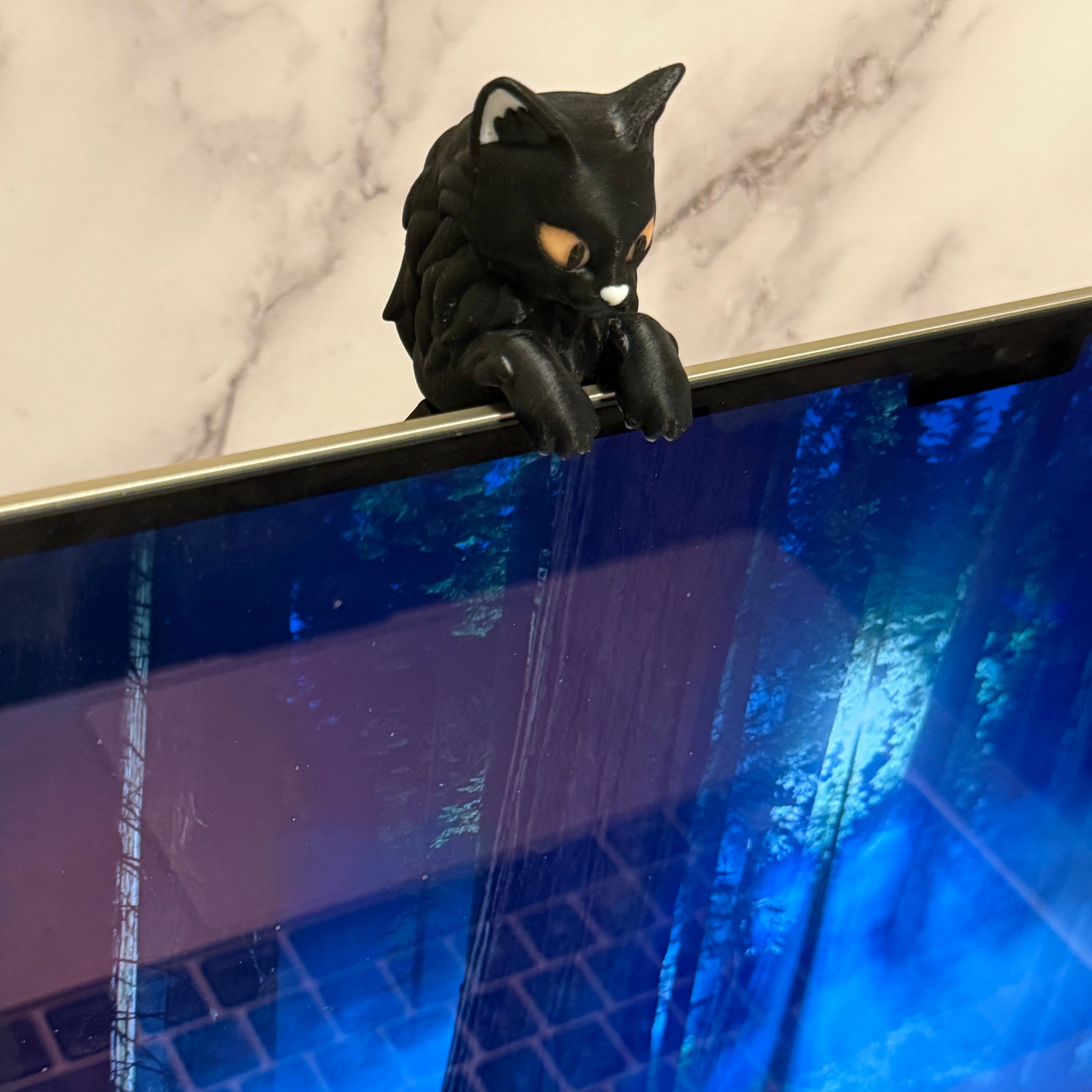 Black cat-shaped figure with orange eyes hanging over the edge of an open laptop screen