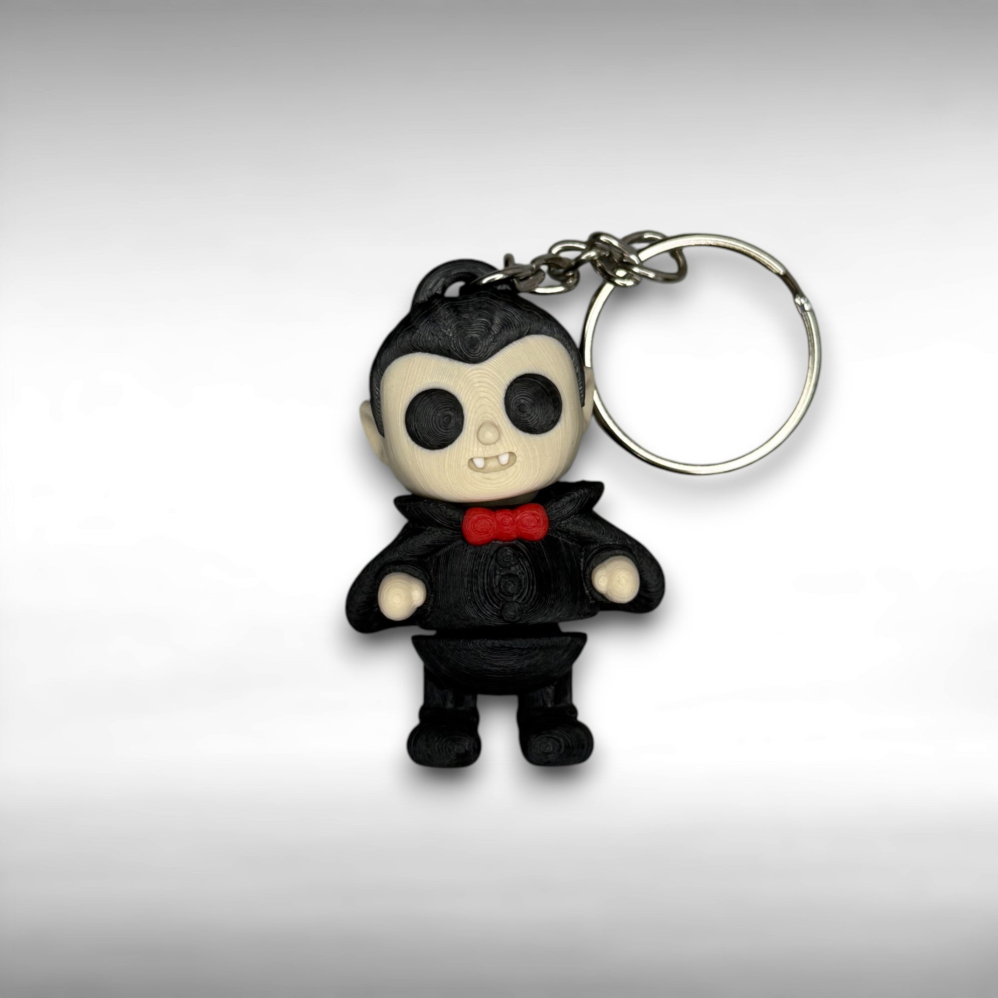 Keychain of a dracula vampire figure with a black cape, white fangs, and a red bowtie on a gray background