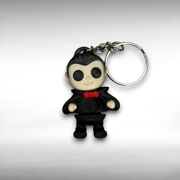 Keychain of a dracula vampire figure with a black cape, white fangs, and a red bowtie on a gray background