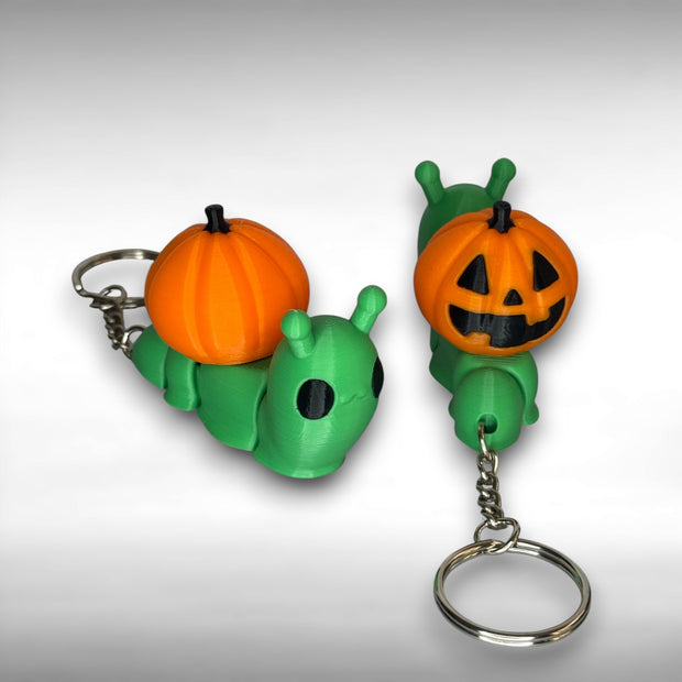 Two green snail-shaped keychains with orange jack-o-lantern shells on a gray background.