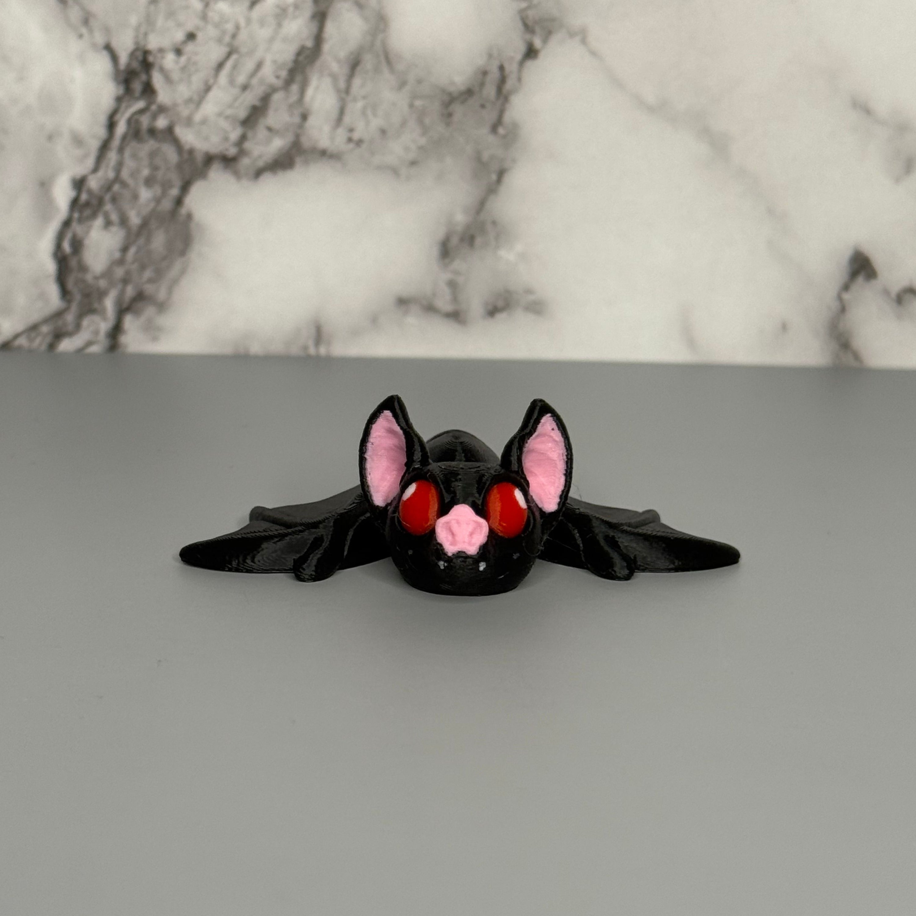 Black bat-shaped figure with red eyes and pink ears on a gray marble  background