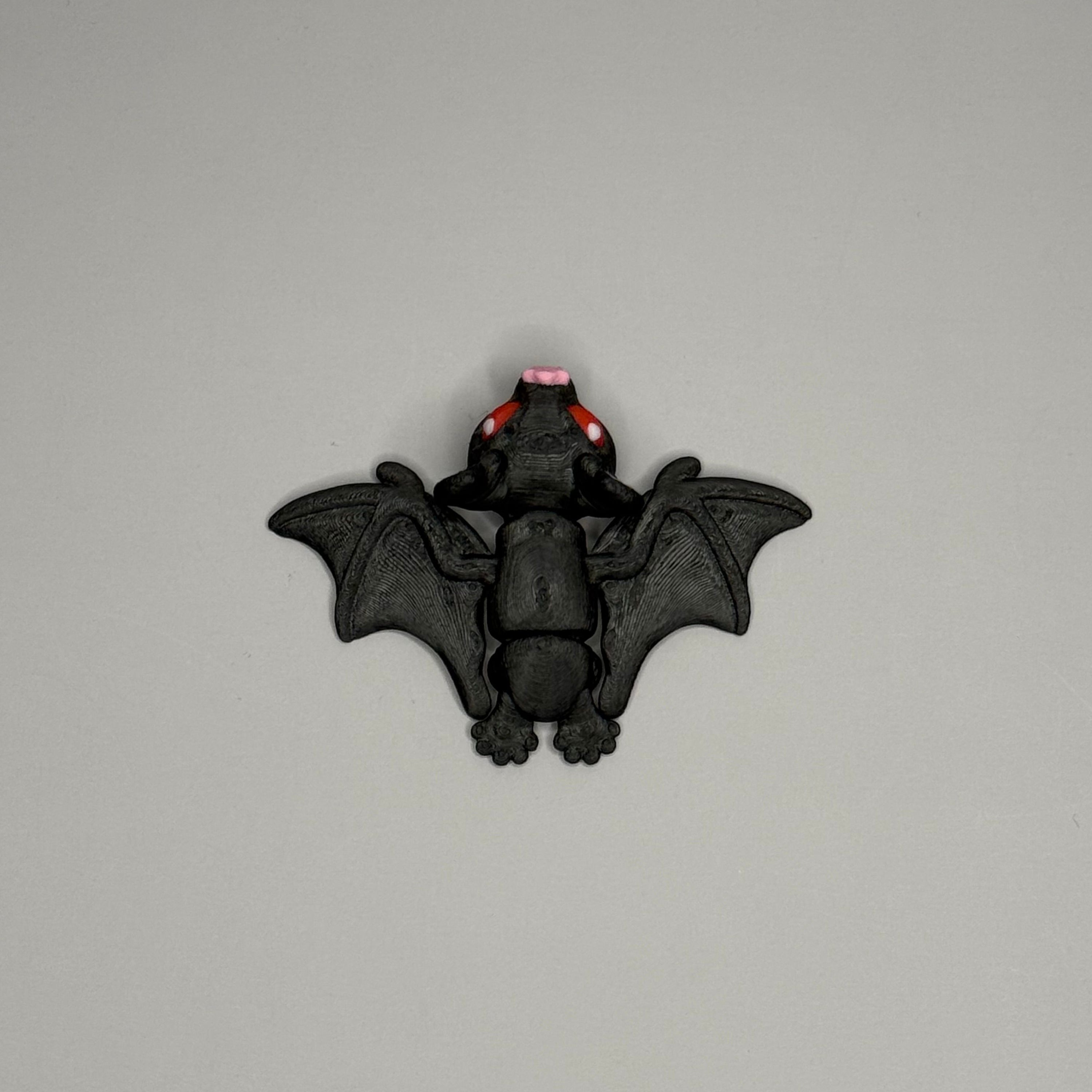 Top side of black bat figurine with red eyes and pink ears on a gray surface with marble background