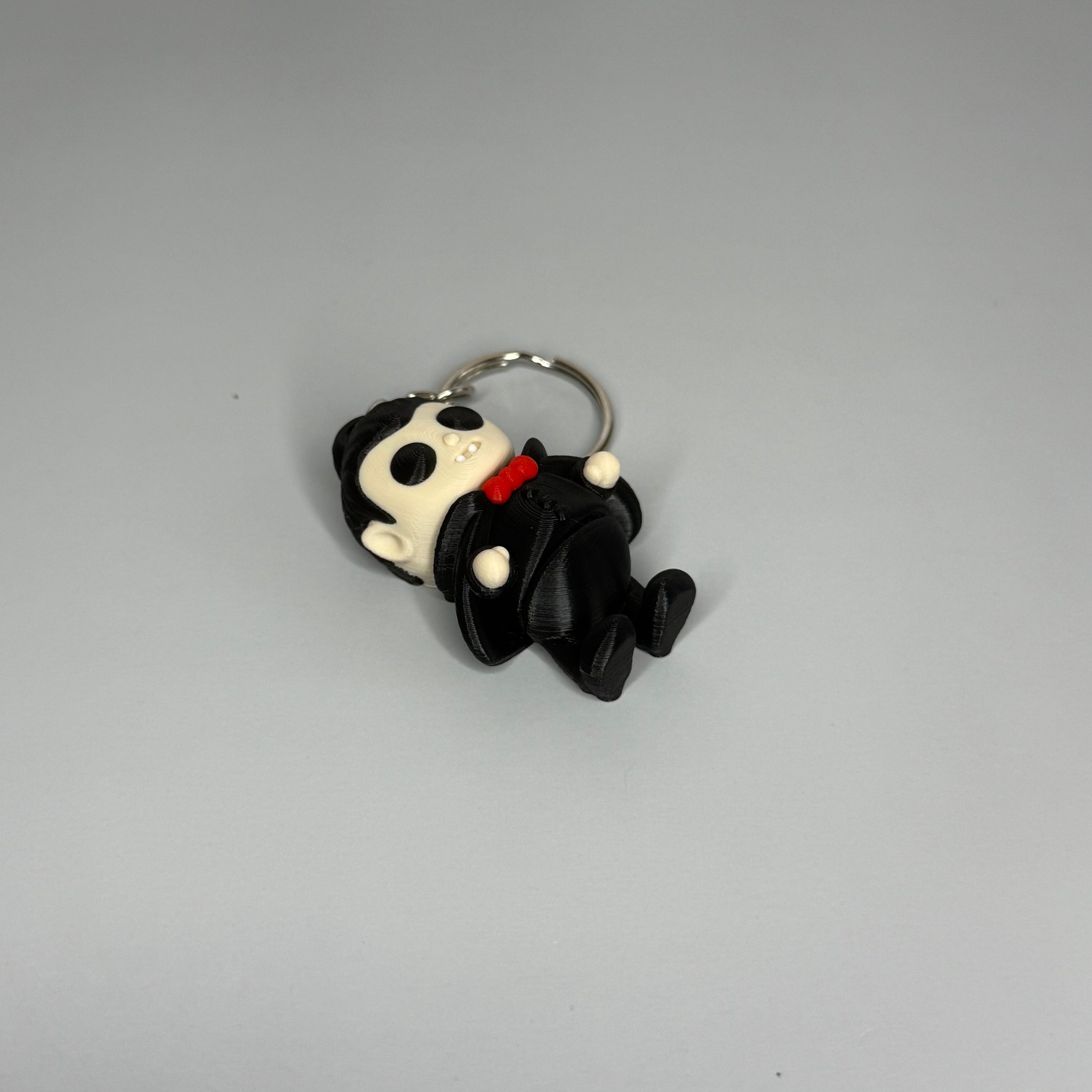 Keychain of a dracula vampire figure with a black cape, white fangs, and a red bowtie on a gray marble background