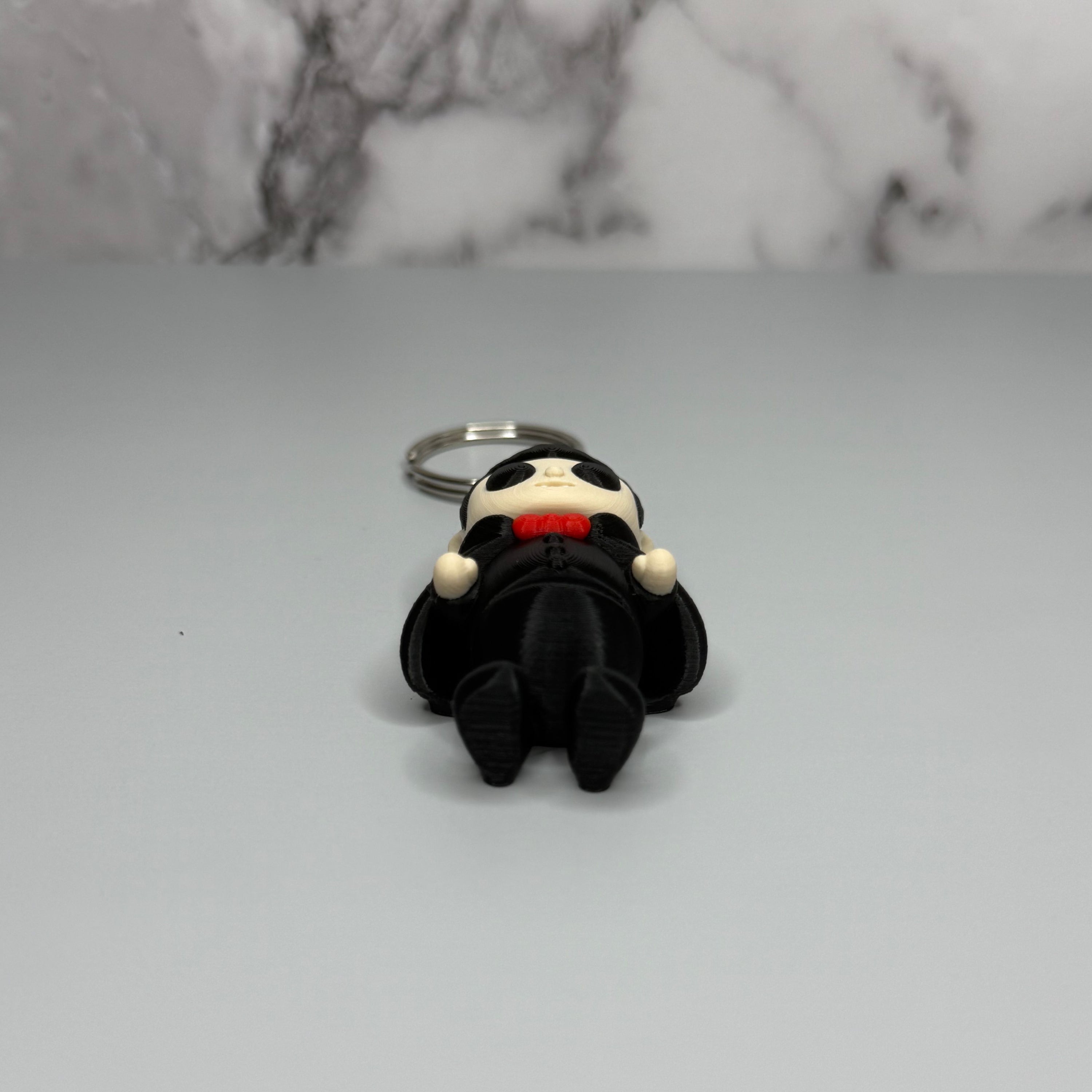 Keychain of a dracula vampire figure with a black cape, white fangs, and a red bowtie on a gray marble background