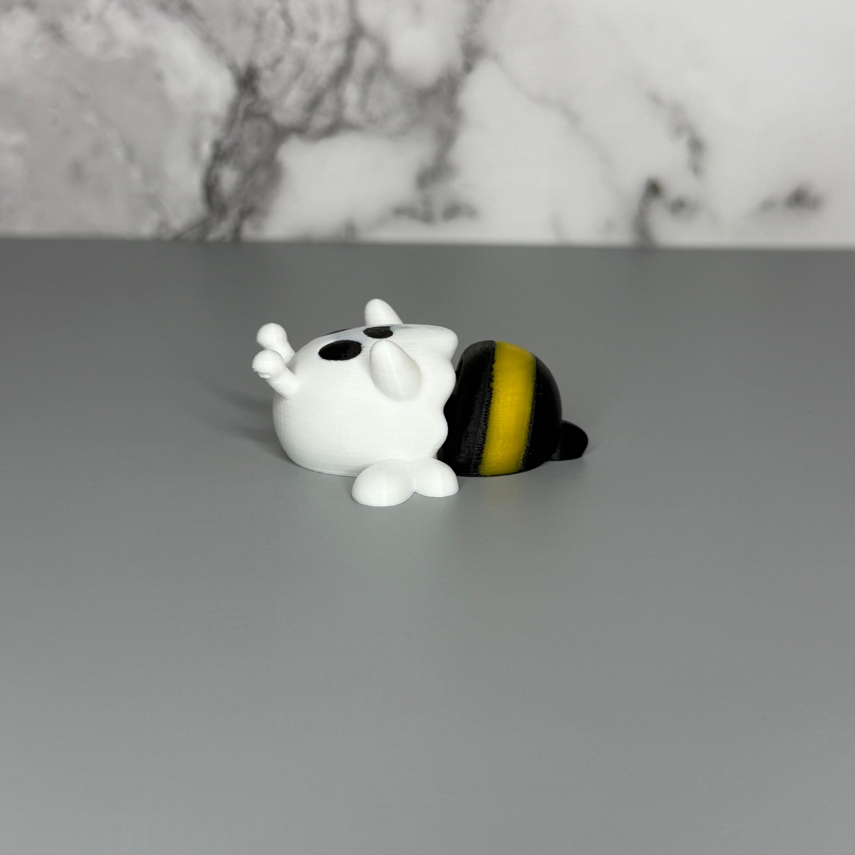 Ghost shaped figure with white wings and a black and yellow bee-shaped lower body on a gray marble  background.
