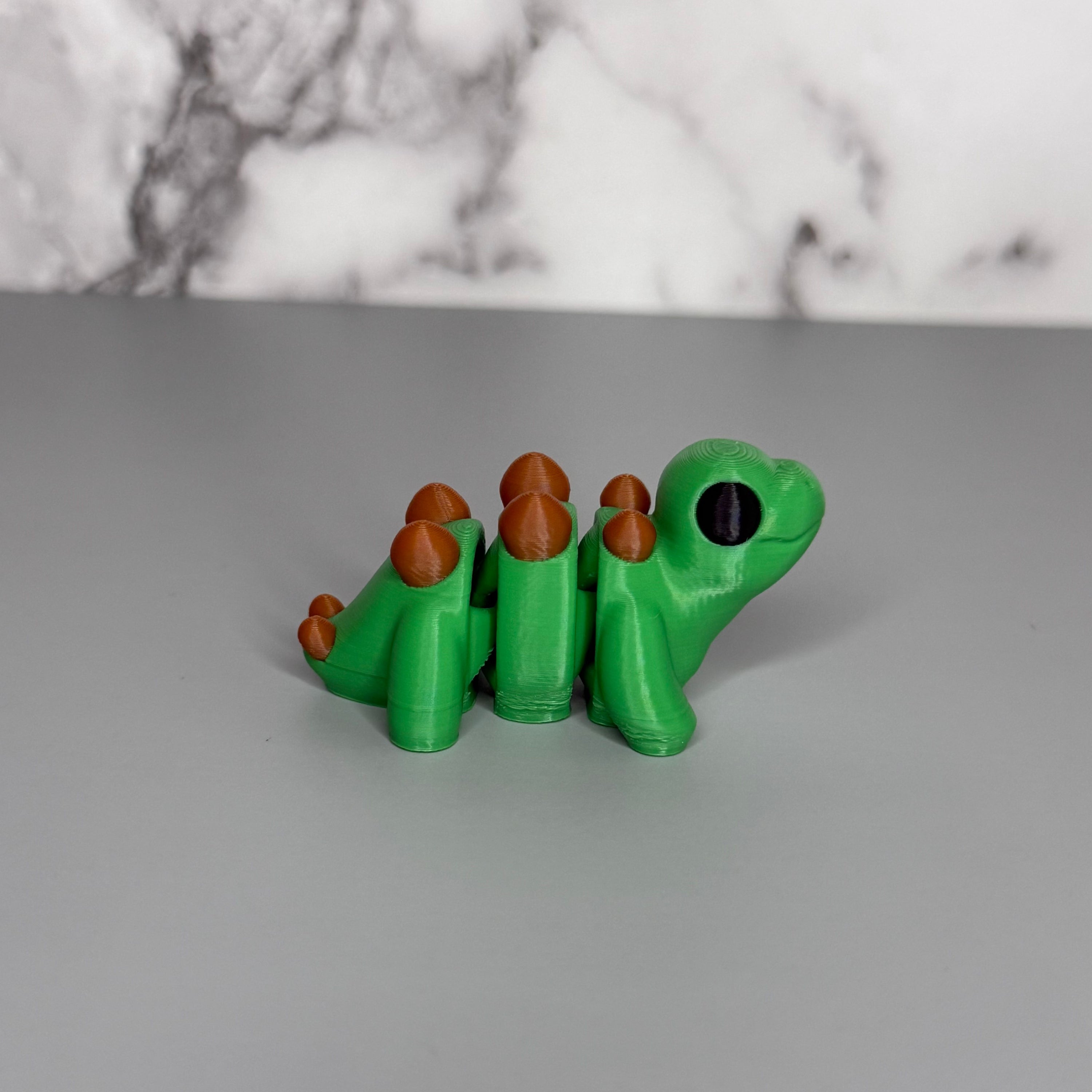 Green dinosaur with brown bumps down its back and tail on a gray marble background