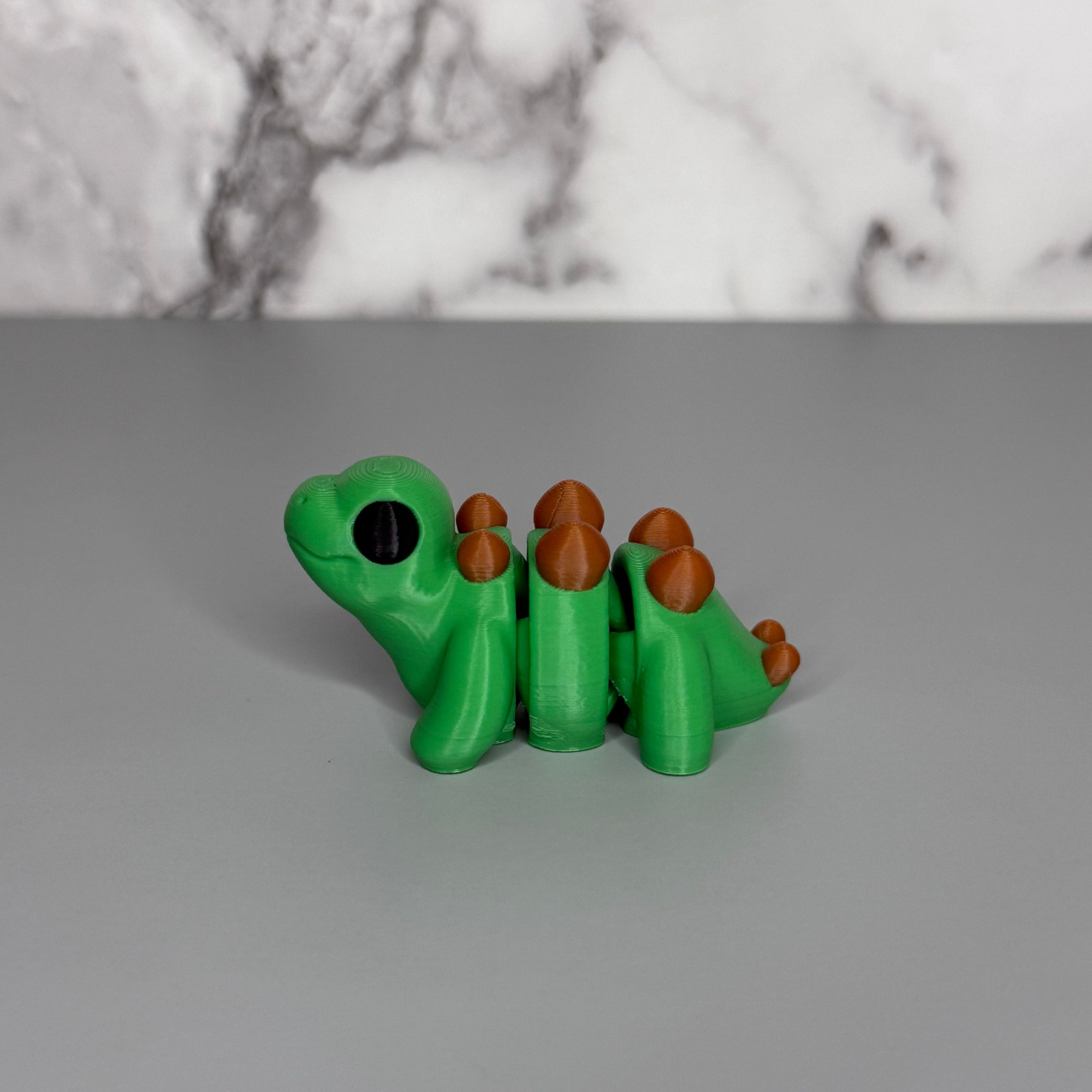 Green dinosaur-shaped object with brown spikes on a gray surface and marble gray background
