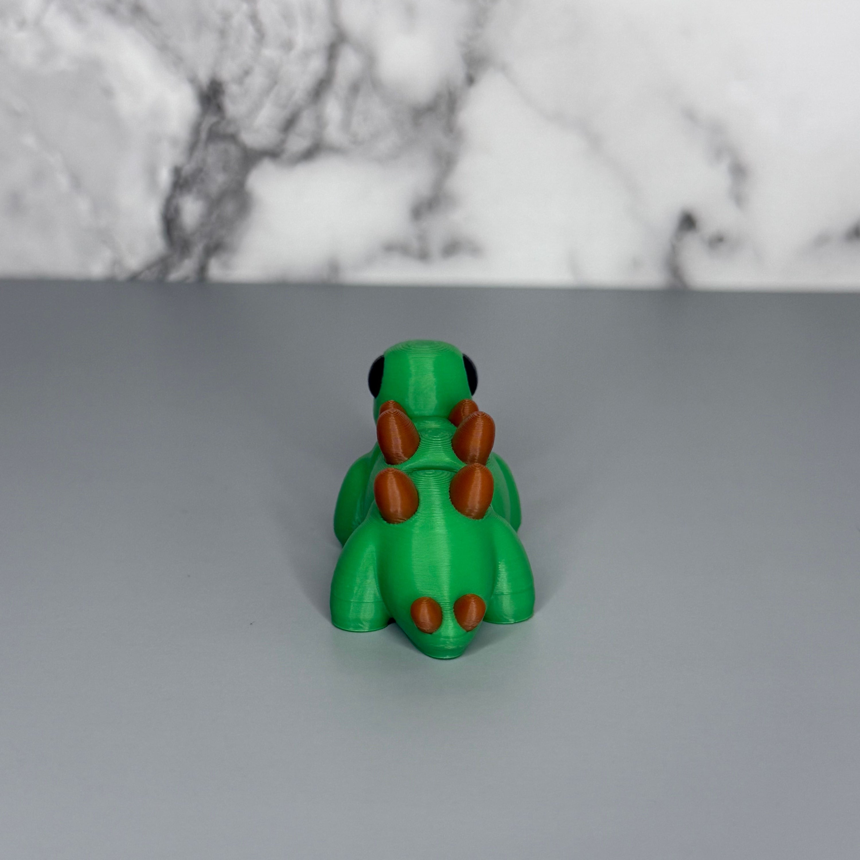 Green dinosaur-shaped object with brown spikes on a gray surface and marble gray background