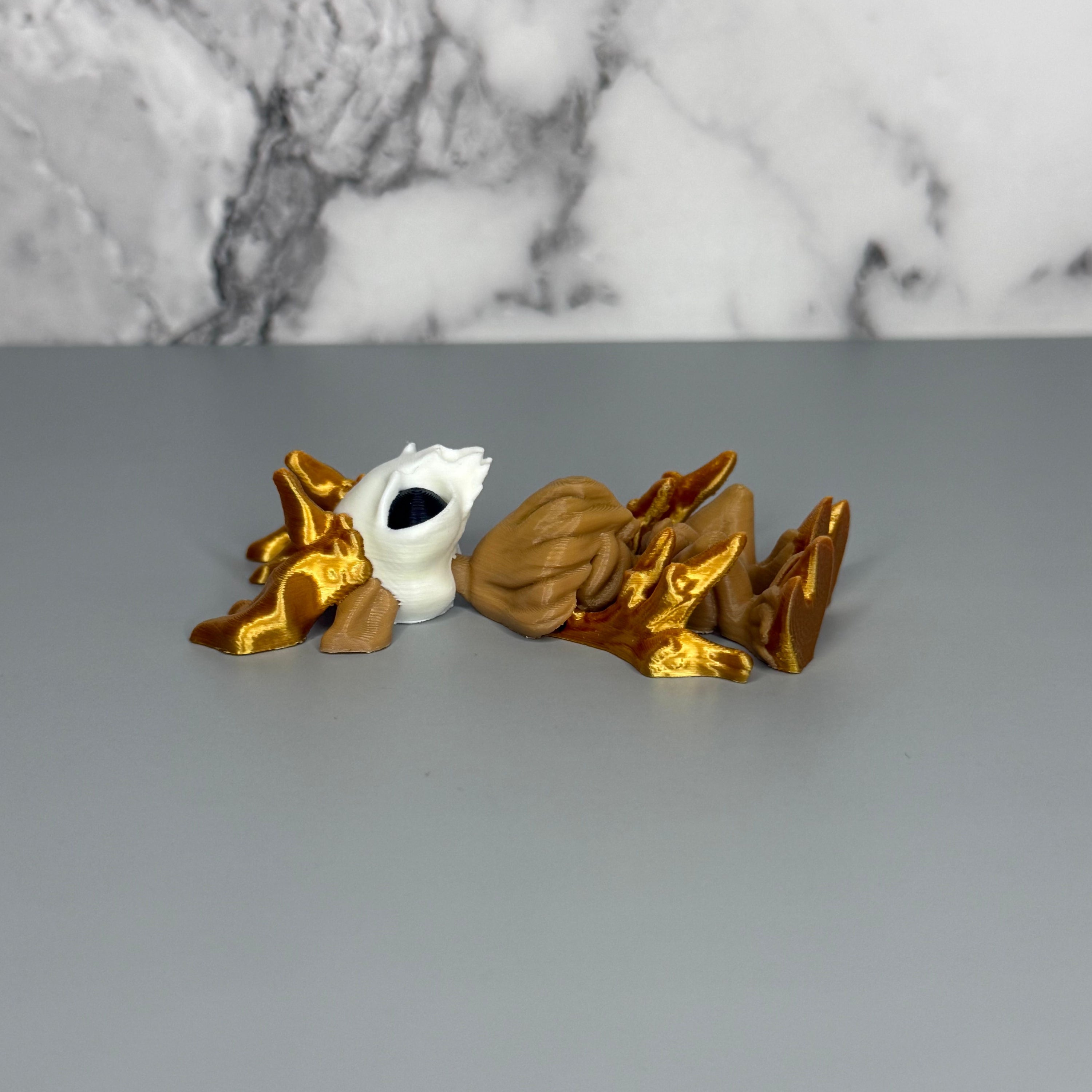 Left side of a figure of a wendigo with gold antlers, white face, brown body, and gold hands and hooves on a gray marble background.