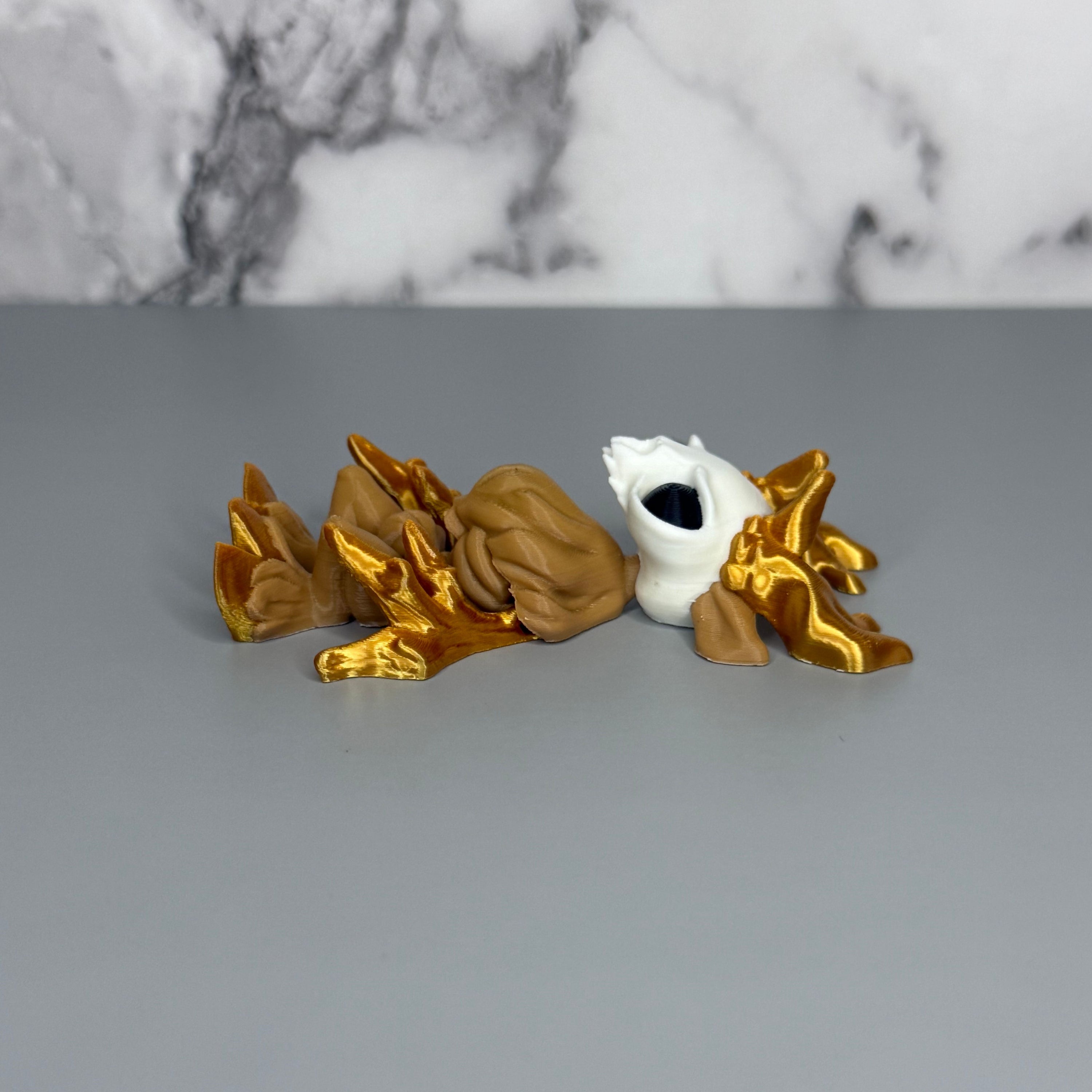 Right side of a figure of a wendigo with gold antlers, white face, brown body, and gold hands and hooves on a gray marble background.