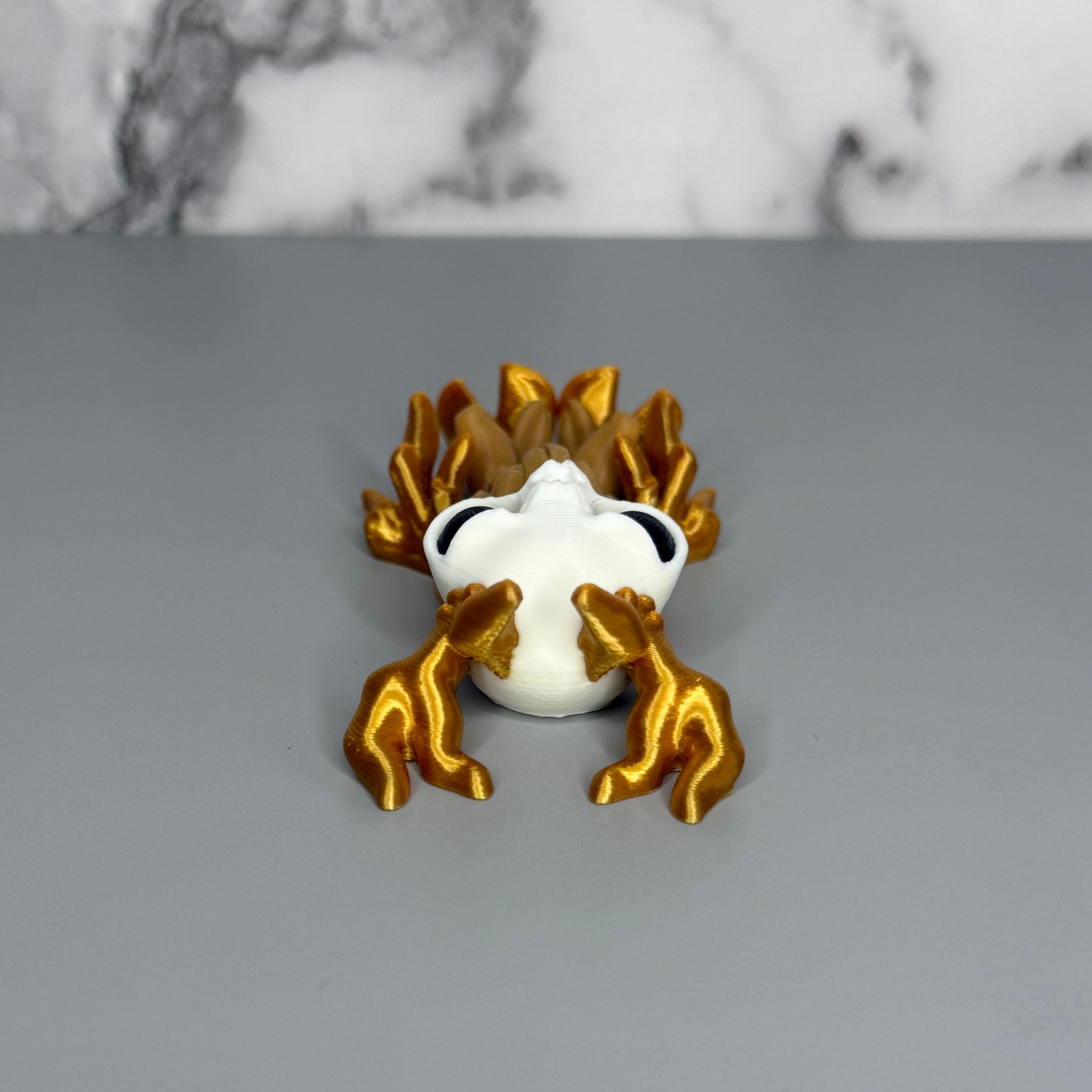 Top side of a figure of a wendigo with gold antlers, white face, brown body, and gold hands and hooves on a gray marble background.