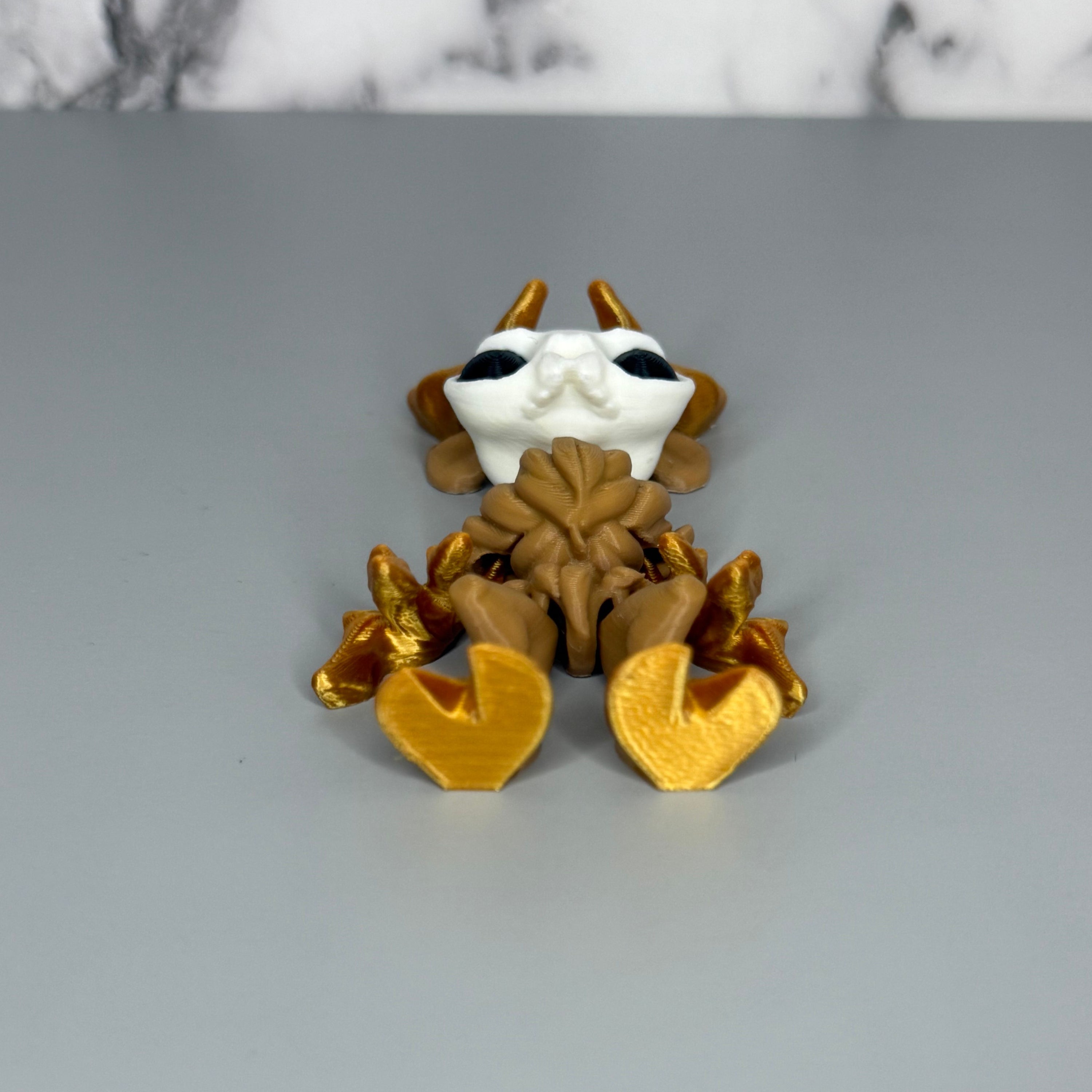 Left side of a figure of a wendigo with gold antlers, white face, brown body, and gold hands and hooves on a gray marble background.