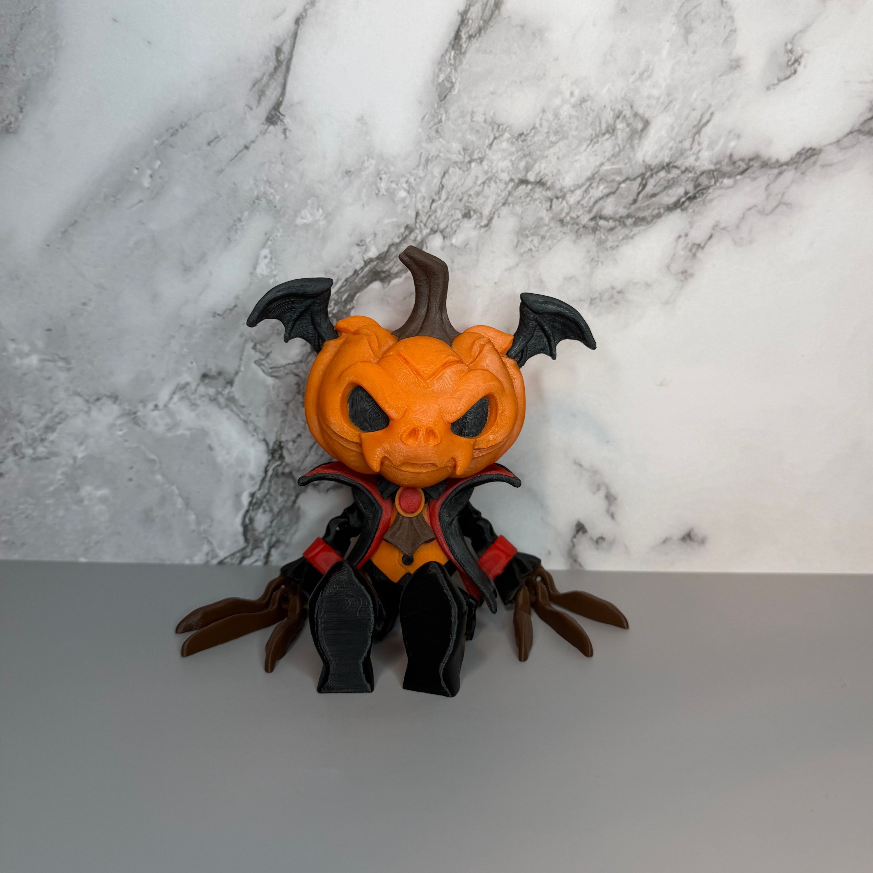 Figure with a head of a pumpkin with bat wings on it, black and red suit, black shoes, and long brown fingers sitting against a gray marbled background