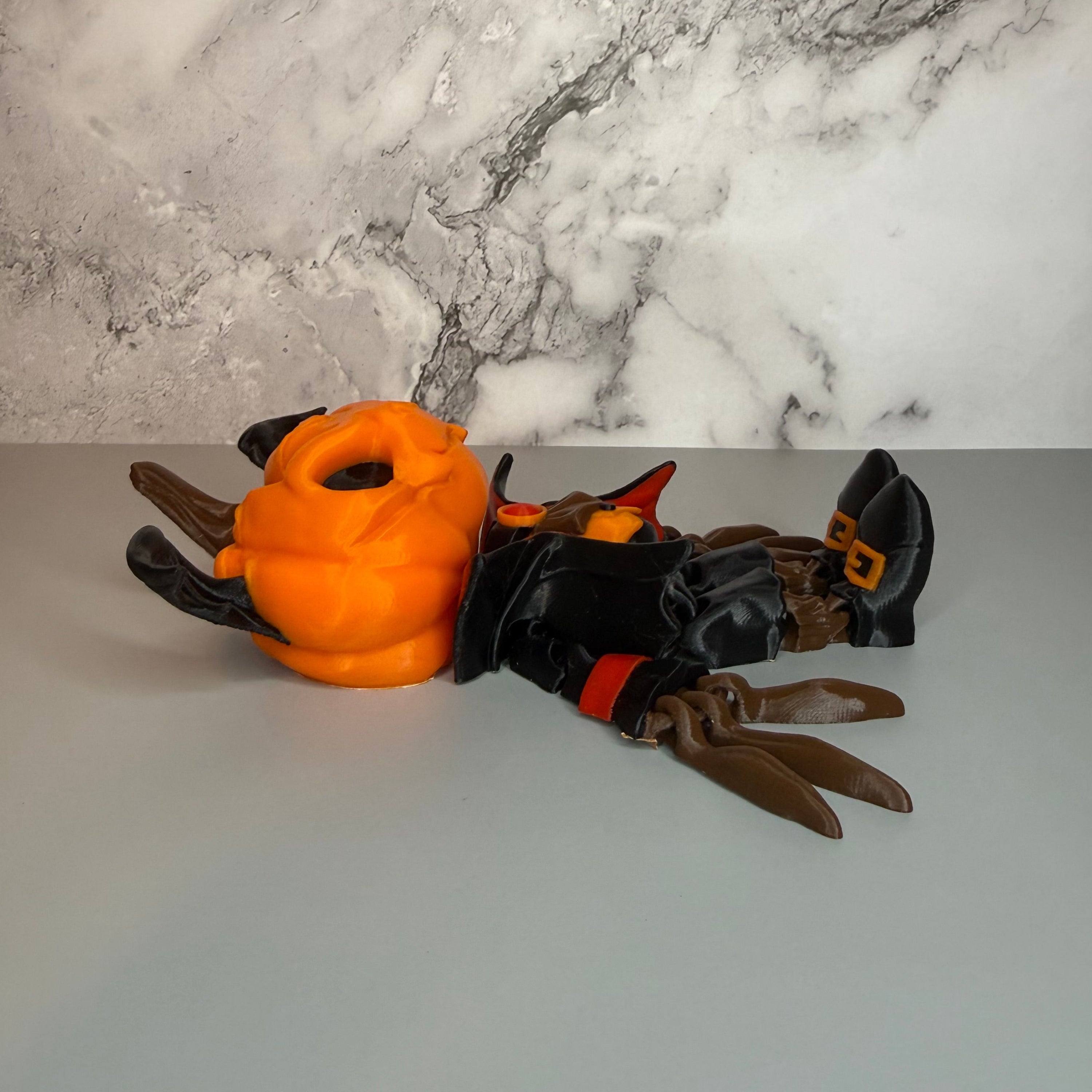 Side view of a figure with a head of a pumpkin with bat wings on it, black and red suit, black shoes with orange buckles, and long brown fingers on a gray and marble background