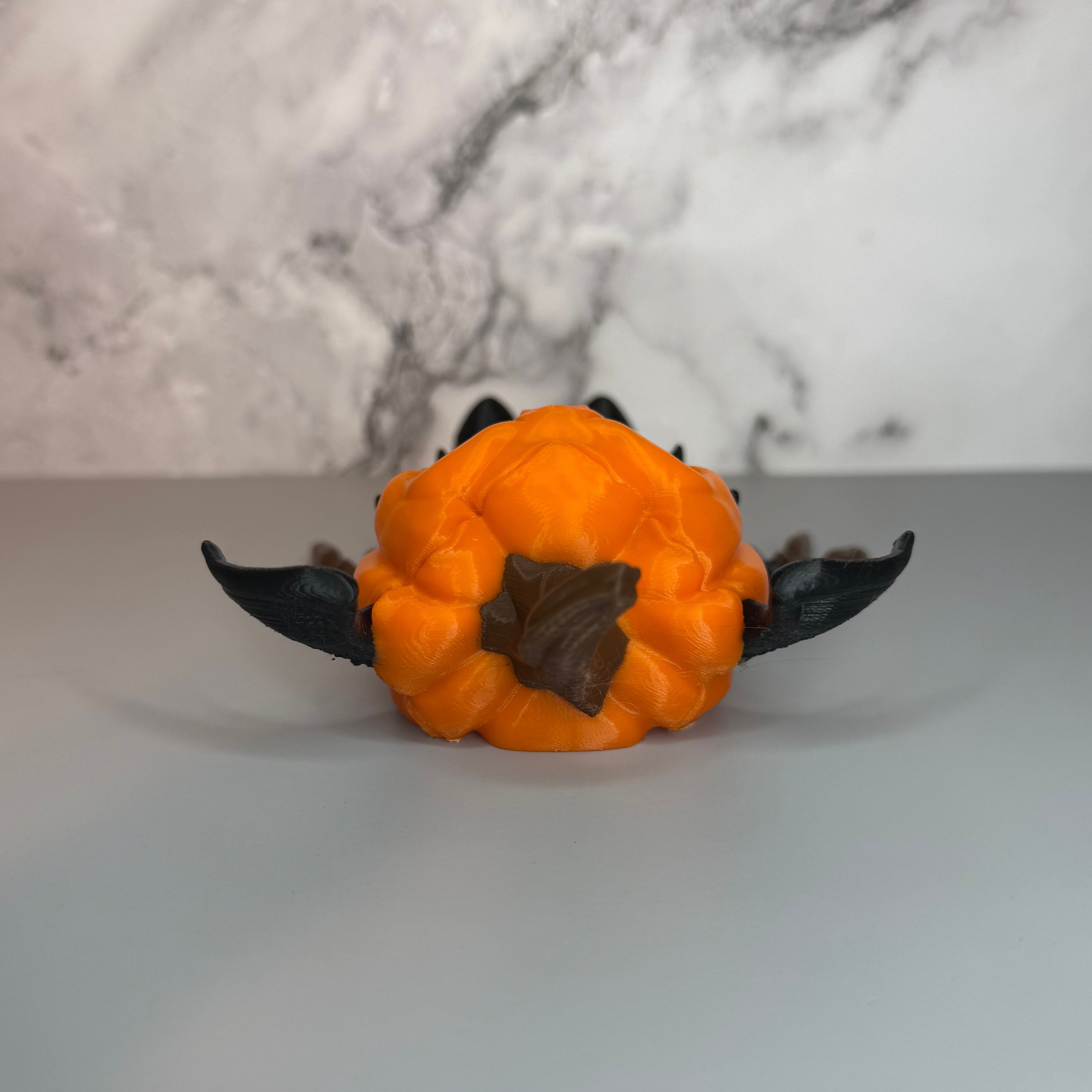 Top view of figurine with pumpkin head with a brown stem and bat wings on a gray marble background.