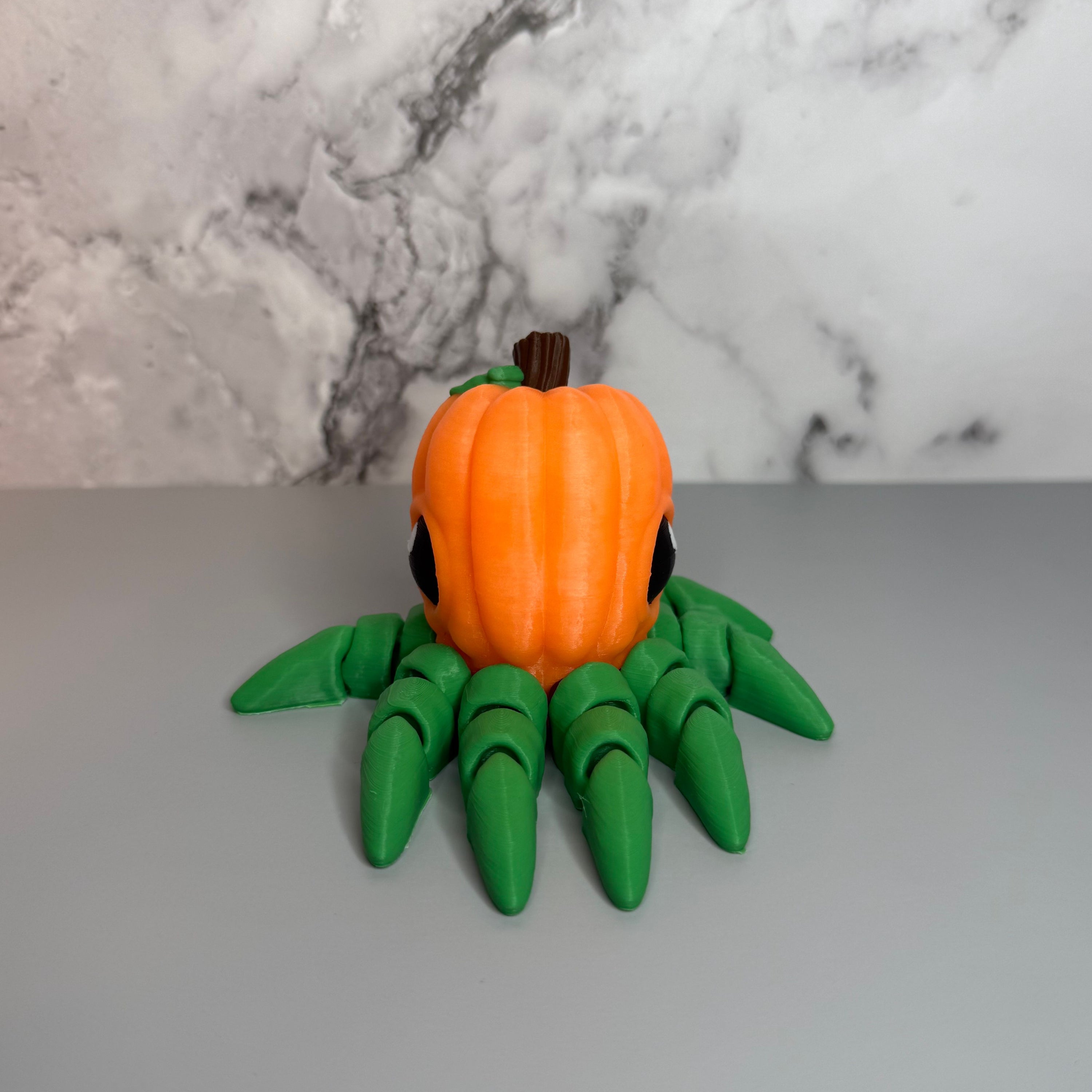 Octopus shaped orange pumpkin figure with green legs on a gray marble background.