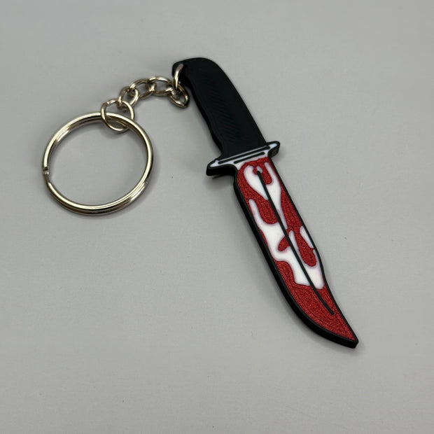 Keychain resembling a knife with a blood-stained blade on a gray background