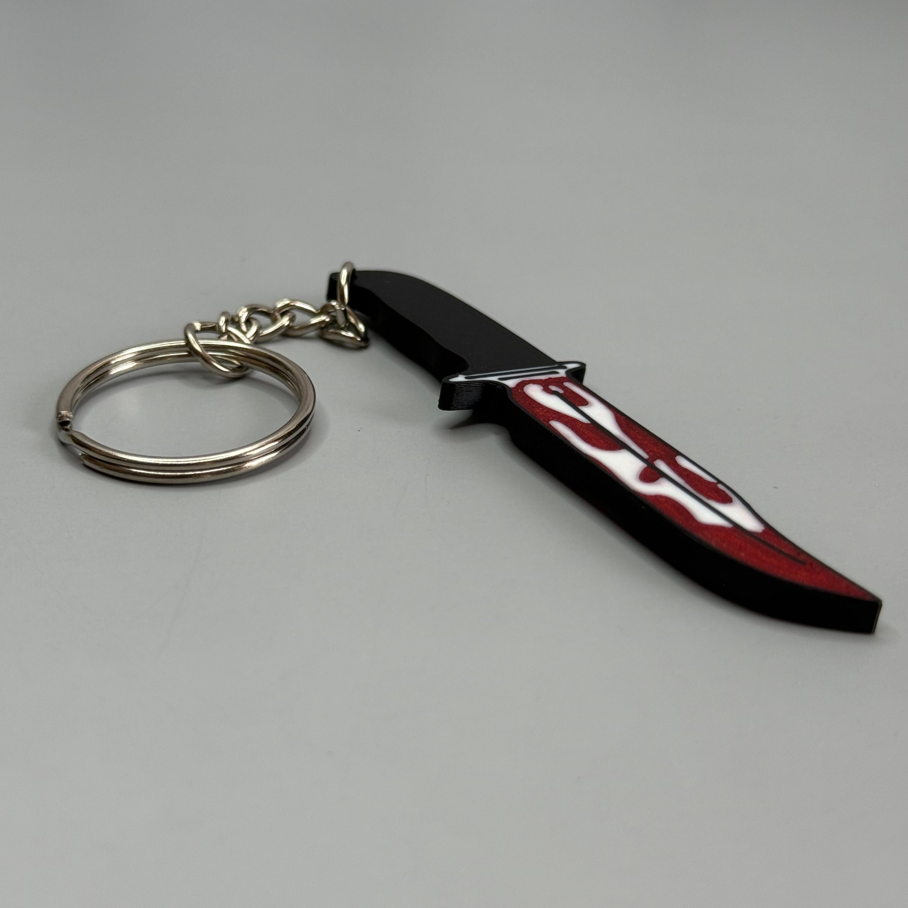 Keychain resembling a knife with a blood-stained blade on a gray background