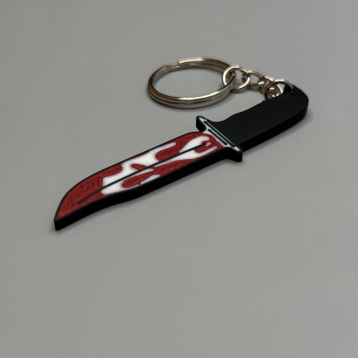 Keychain resembling a knife with a blood-stained blade on a gray background