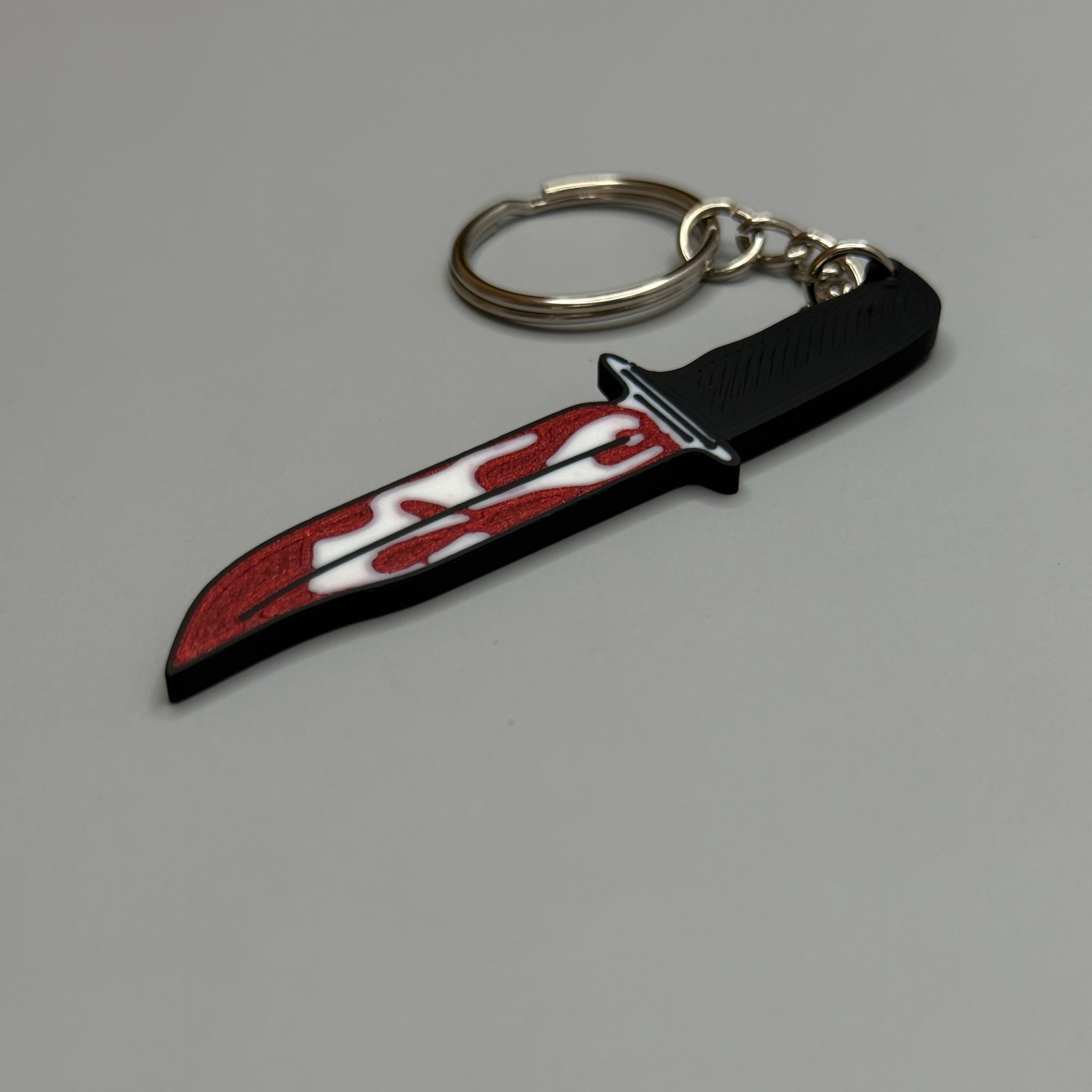 Keychain resembling a knife with a blood-stained blade on a gray background