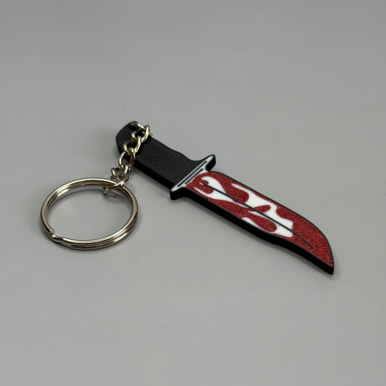 Keychain resembling a knife with a blood-stained blade on a gray background