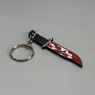 Keychain resembling a knife with a blood-stained blade on a gray background