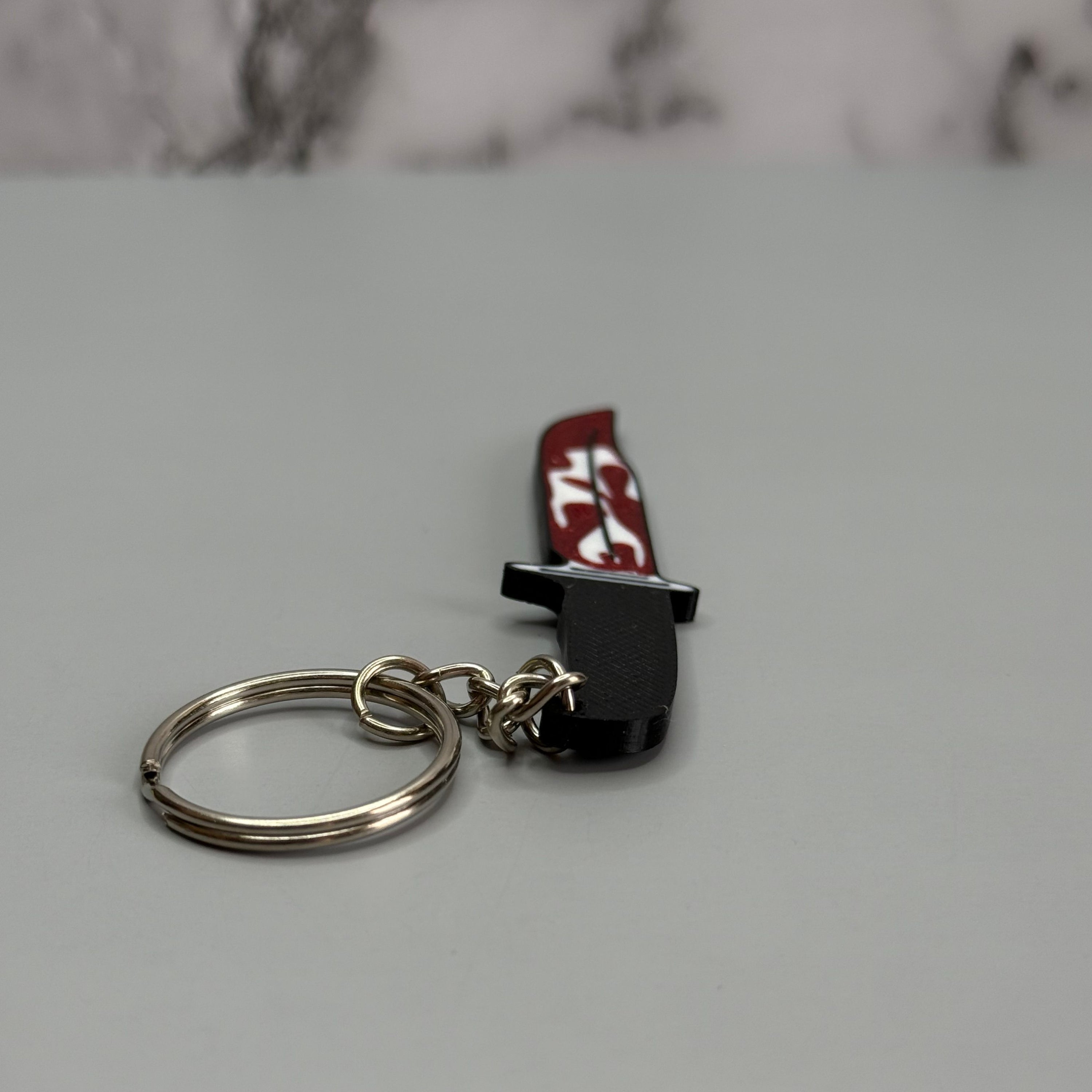 Keychain resembling a knife with a blood-stained blade on a gray background