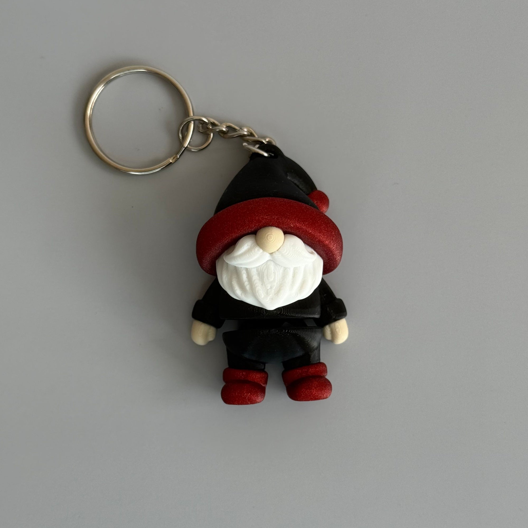 Small gnome keychain with a black and red hat, red shoes, and a white beard on a gray surface