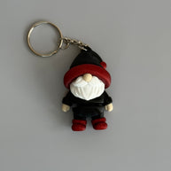 Small gnome keychain with a black and red hat, red shoes, and a white beard on a gray surface