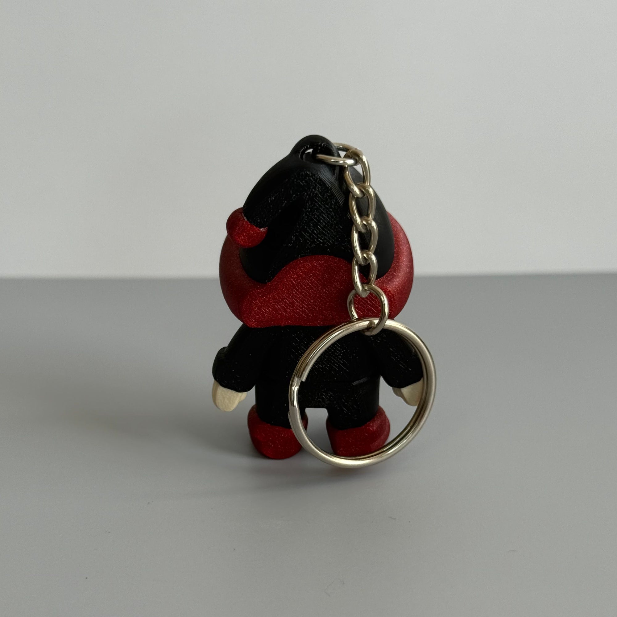 Back perspective of a small gnome keychain with a black and red hat with red shoes on a gray surface
