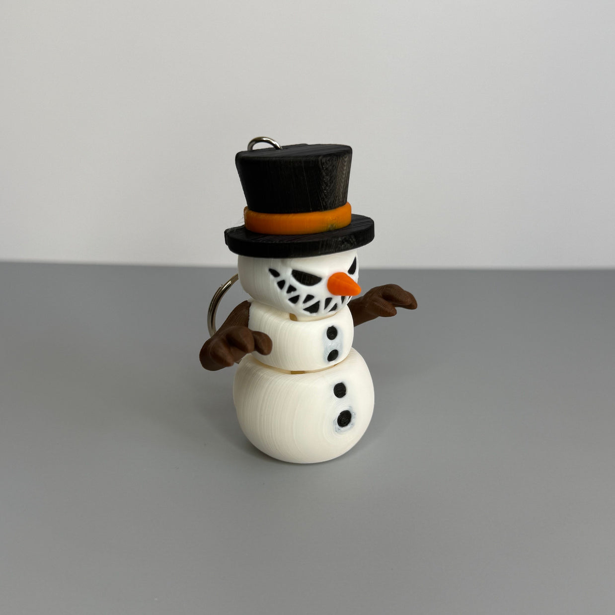 Keychain of a small snowman with a sinister smile with black top hat on a gray background