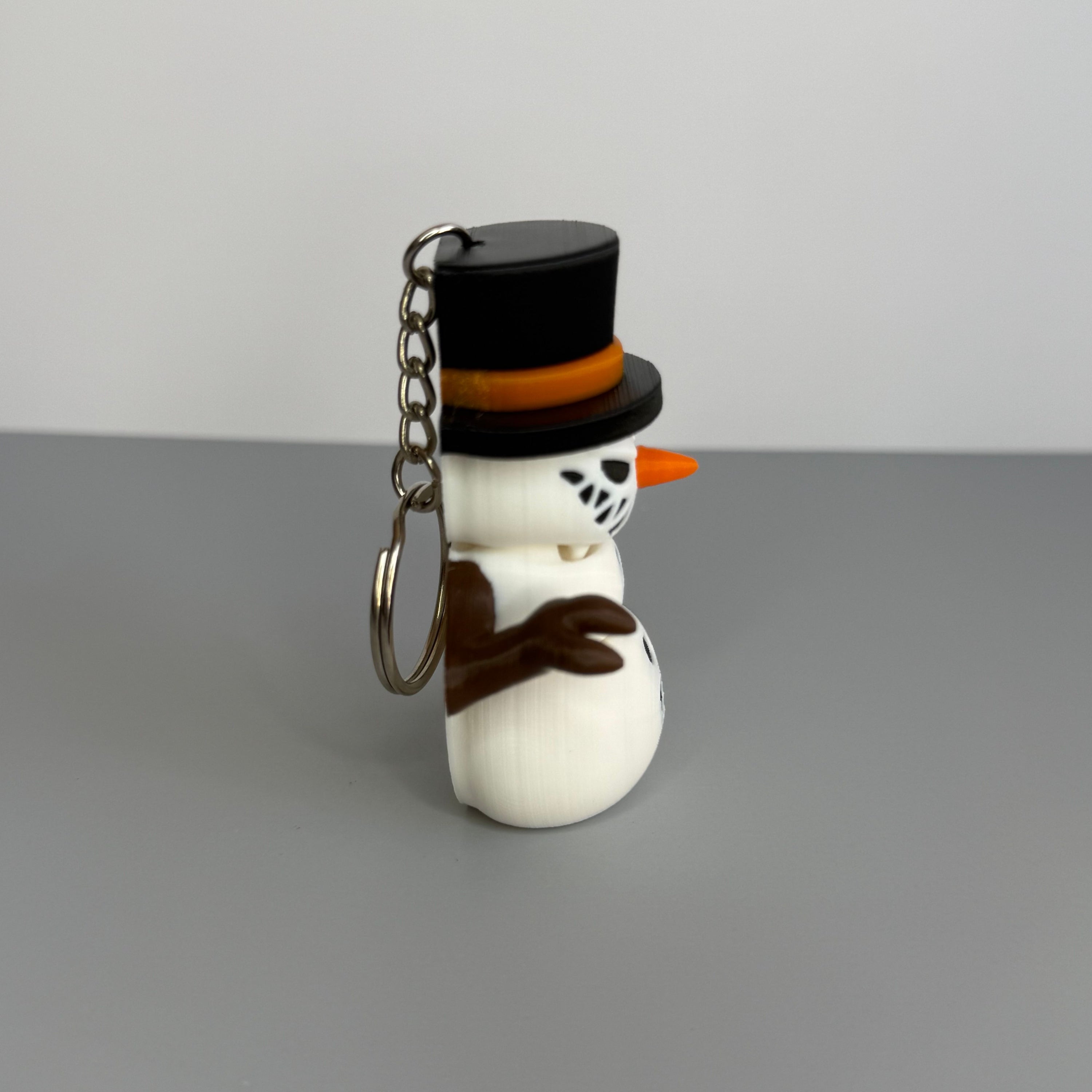 Left side of a keychain of a small snowman with a sinister smile with black top hat on a gray background