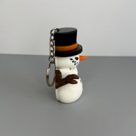 Left side of a keychain of a small snowman with a sinister smile with black top hat on a gray background