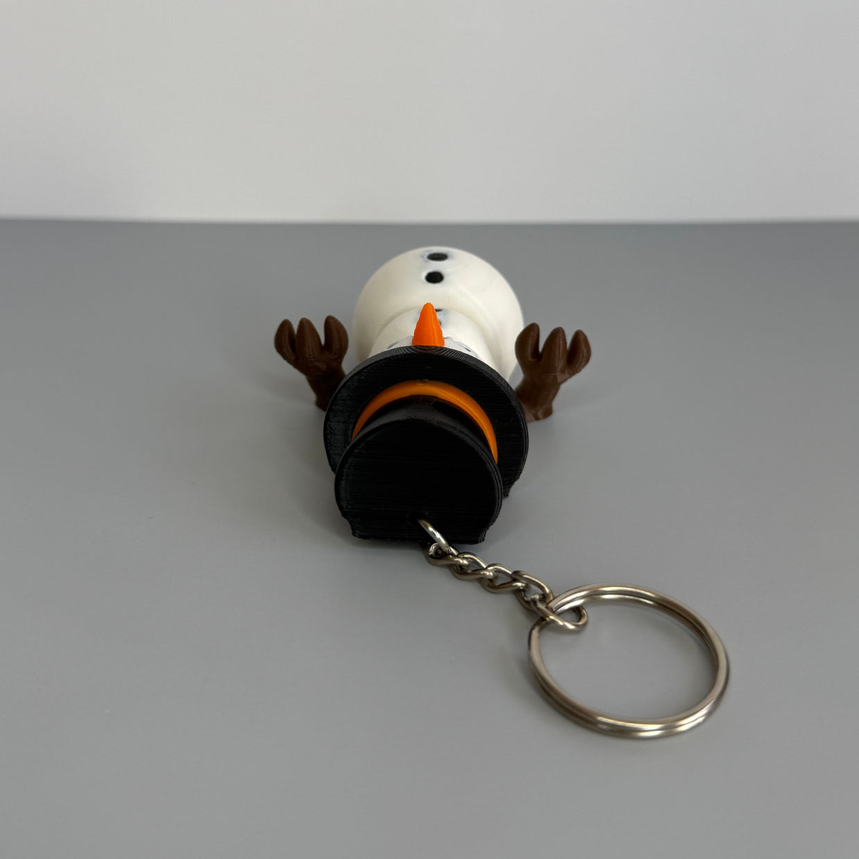 Keychain of a small snowman with black top hat and orange nose on a gray background