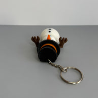 Keychain of a small snowman with black top hat and orange nose on a gray background