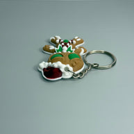 Keychain shaped like a gingerbread man with green eyes, candy cane shaped bowtie, and a Santa hat on a gray background 