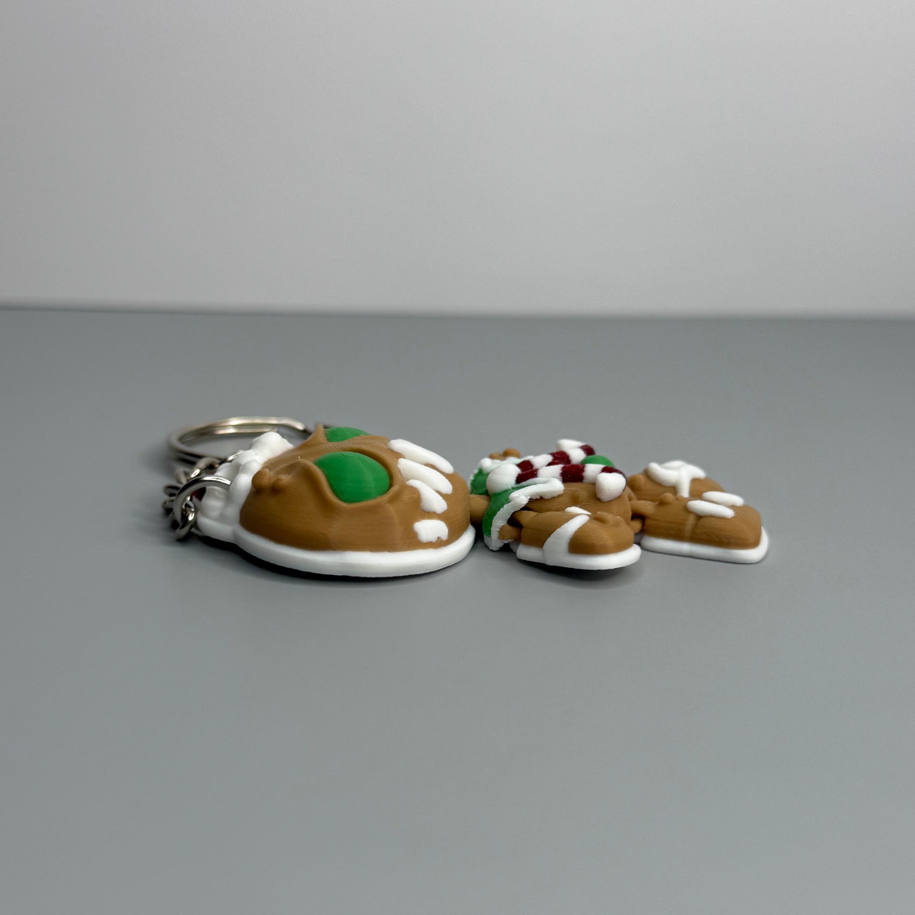 Left side of keychain shaped like a gingerbread man with green eyes, candy cane shaped bowtie, and a Santa hat on a gray background.
