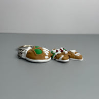 Left side of keychain shaped like a gingerbread man with green eyes, candy cane shaped bowtie, and a Santa hat on a gray background.