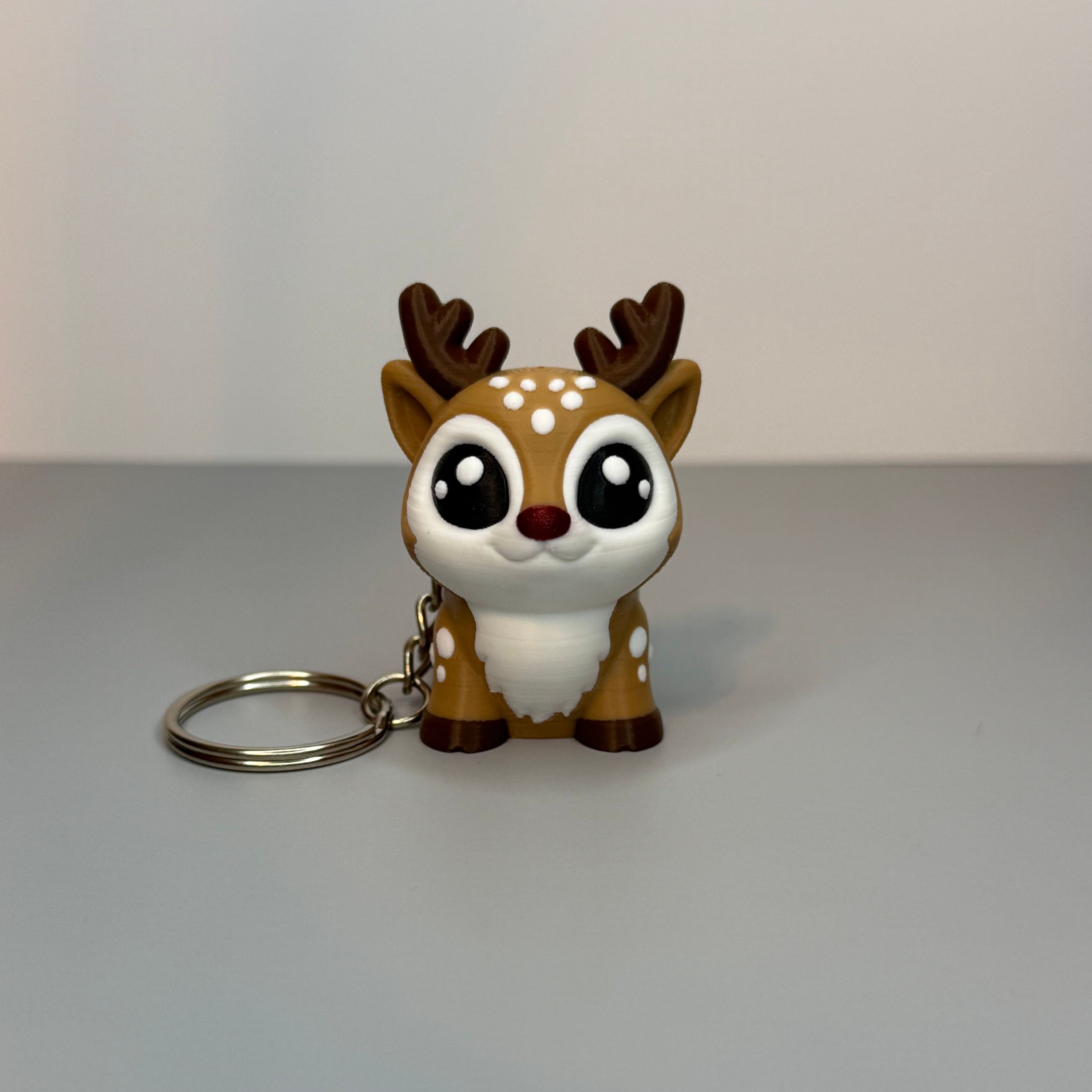 Front perspective of reindeer-shaped keychain with a red, shimmer nose on a gray background. 