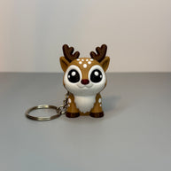 Front perspective of reindeer-shaped keychain with a red, shimmer nose on a gray background. 