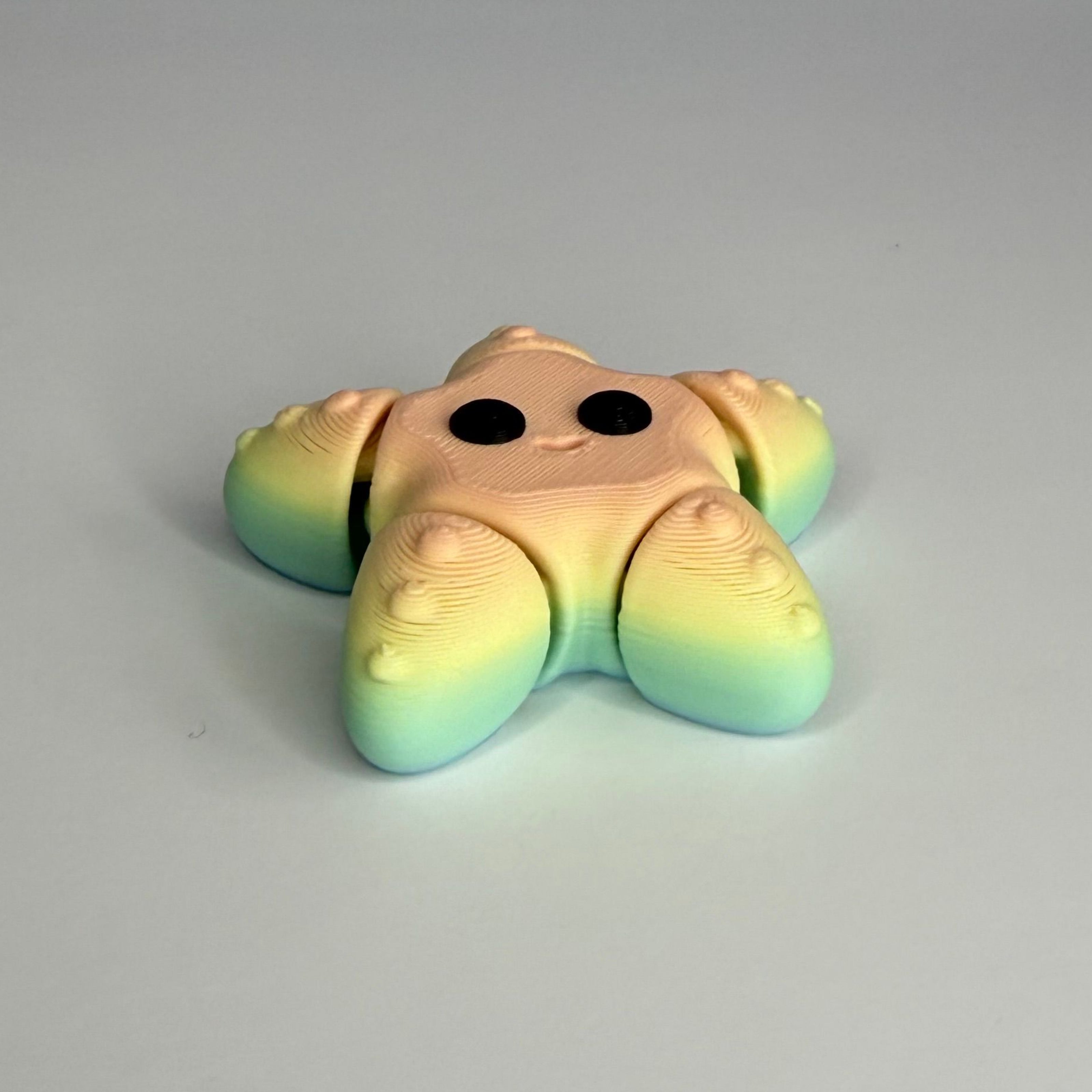Bottom side of smiling star-shaped figure with a gradient rainbow color pattern and black eyes on a white background