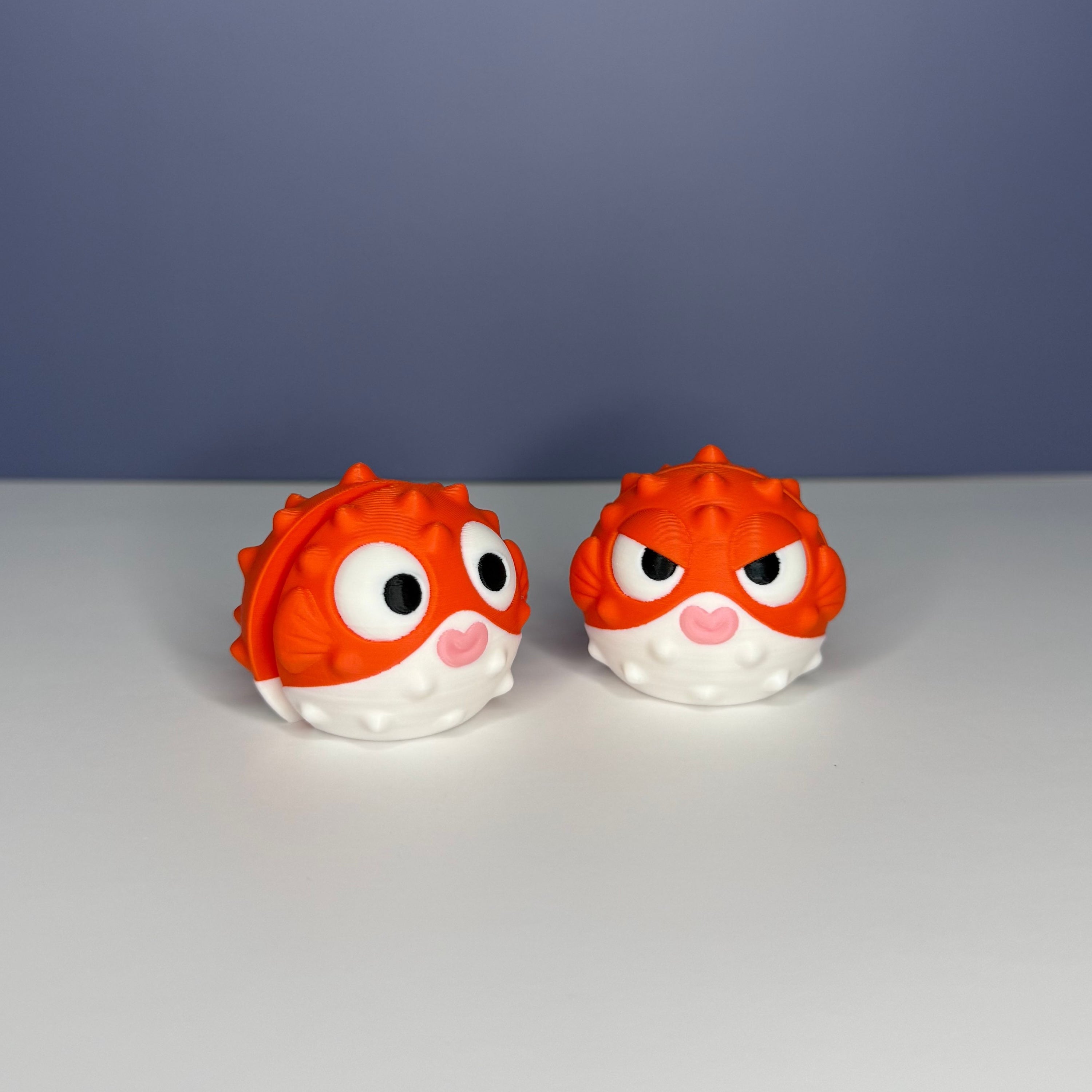 Two orange and white puffer fish figures, one with a circular eyes and one with slanted eyes, on a blue and white background