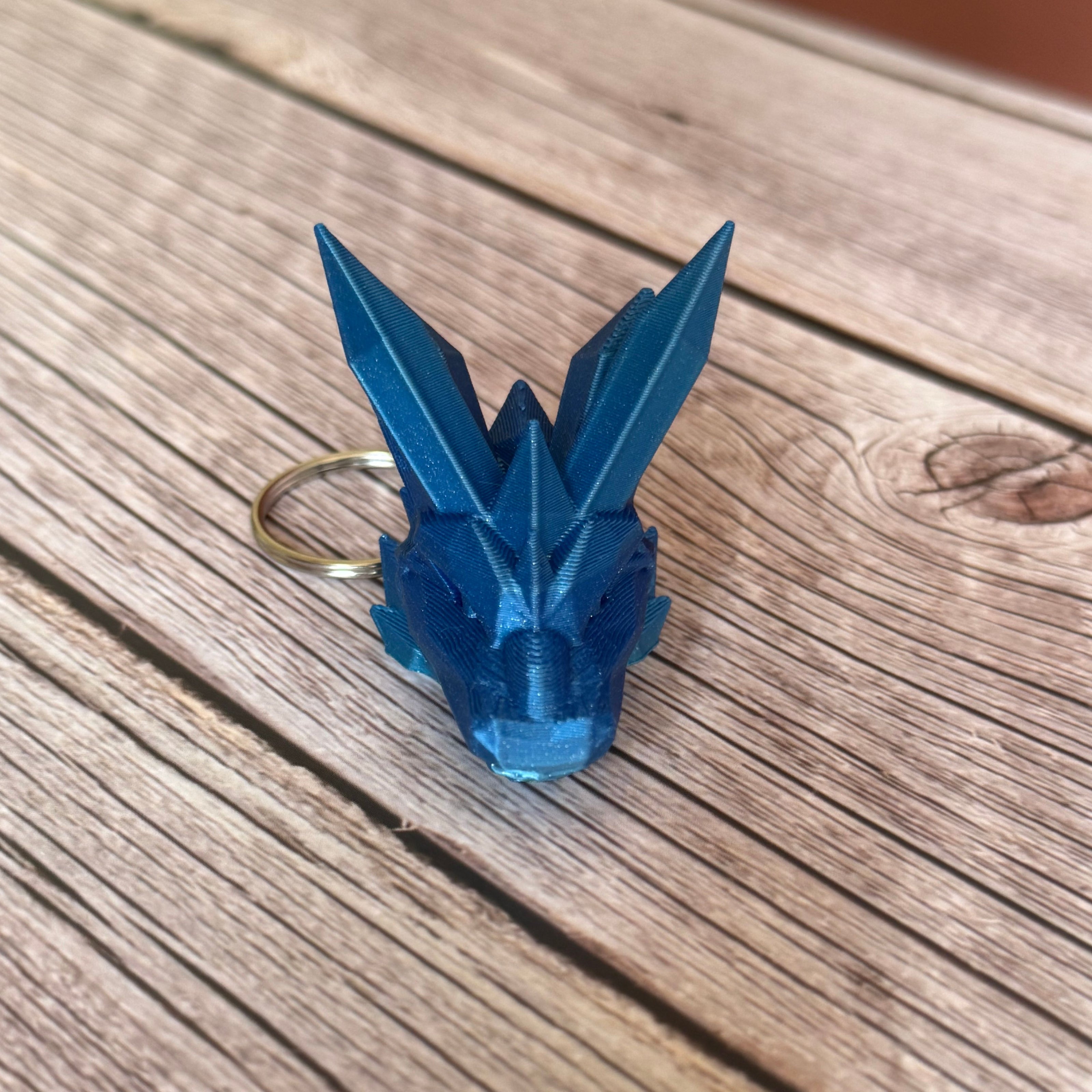 blue 3D printed keychain shaped like a dragon head with crystal-like details, placed on a wooden surface